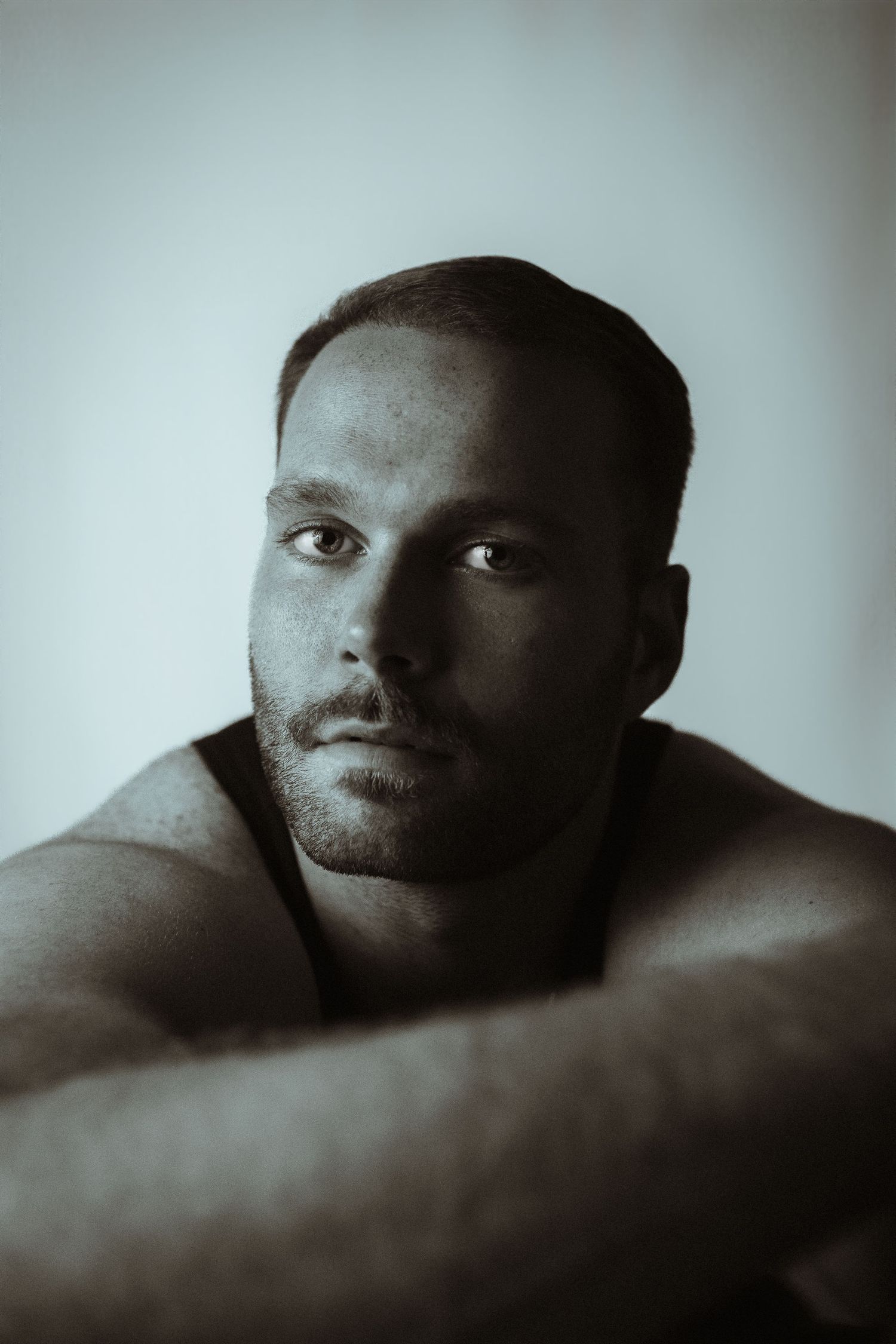 Black and white portrait of a muscular man with short hair and stubble, resting his arms crossed in front of him.