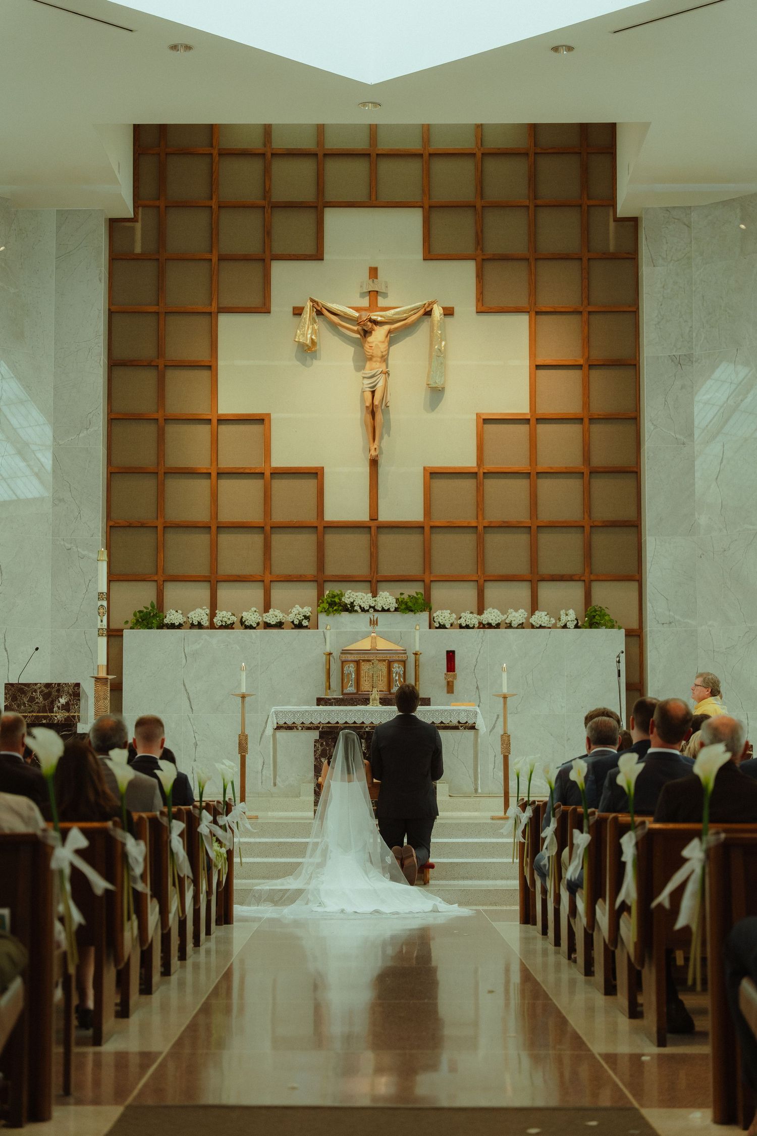 A bride and groom walk down the aisle toward a crucifix altar in an elegant Catholic church wedding ceremony.