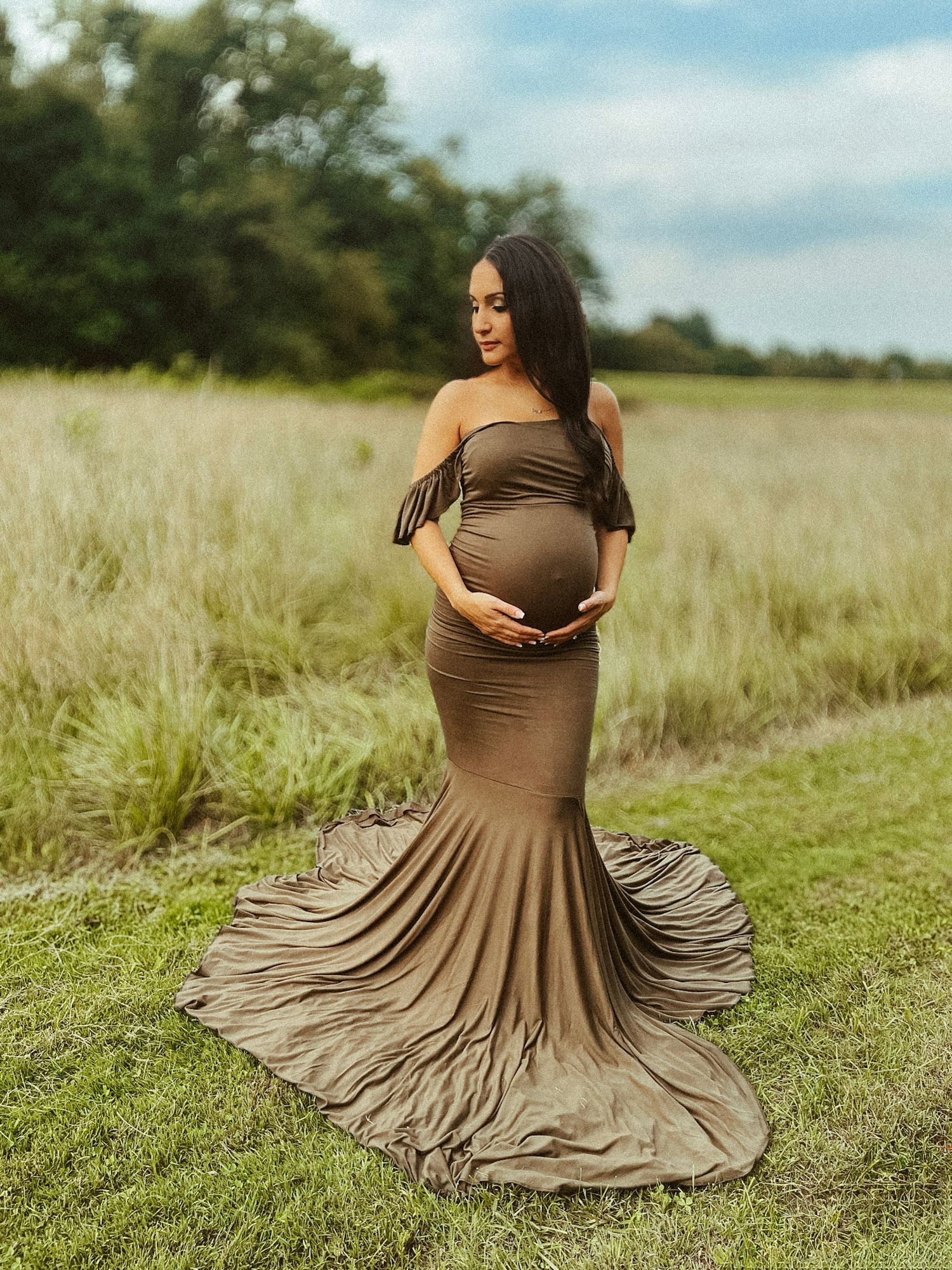 Intimate outdoor maternity session featuring a mother-to-be posing in a natural landscape, captured with soft, airy lighting.