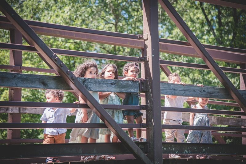 Family of four sharing a joyful moment on a rustic wooden bridge, captured in natural light by Covered in Faith Photography.