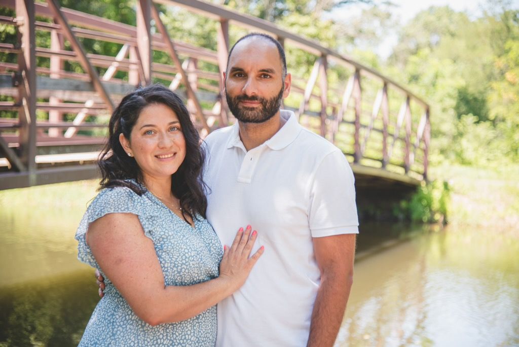 A loving couple embracing on a rustic wooden bridge, captured in an airy and romantic outdoor portrait by Covered in Faith Photography.