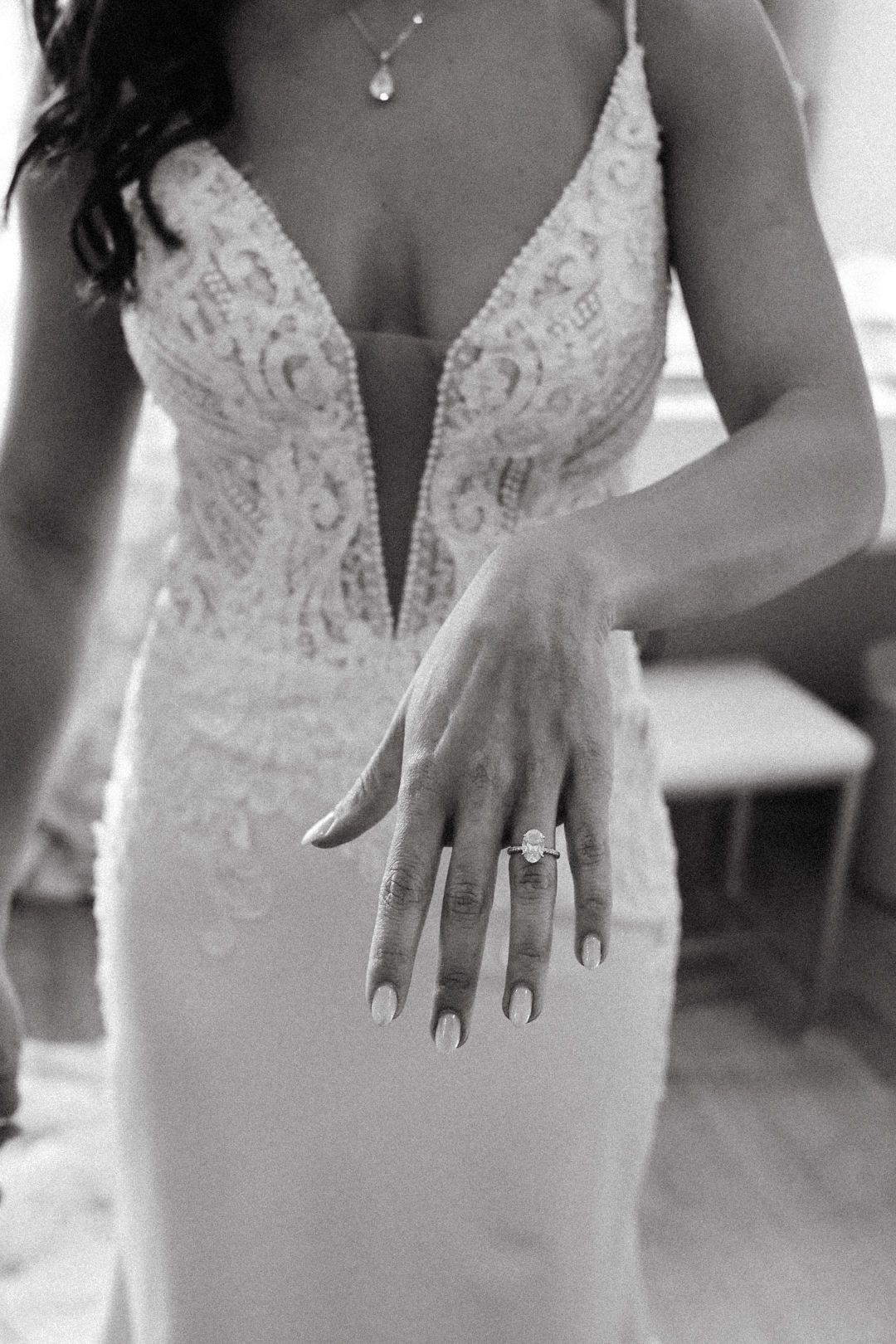 Intimate close-up of a bride’s hand, showcasing her sparkling engagement ring and the intricate lace details of her dress.
