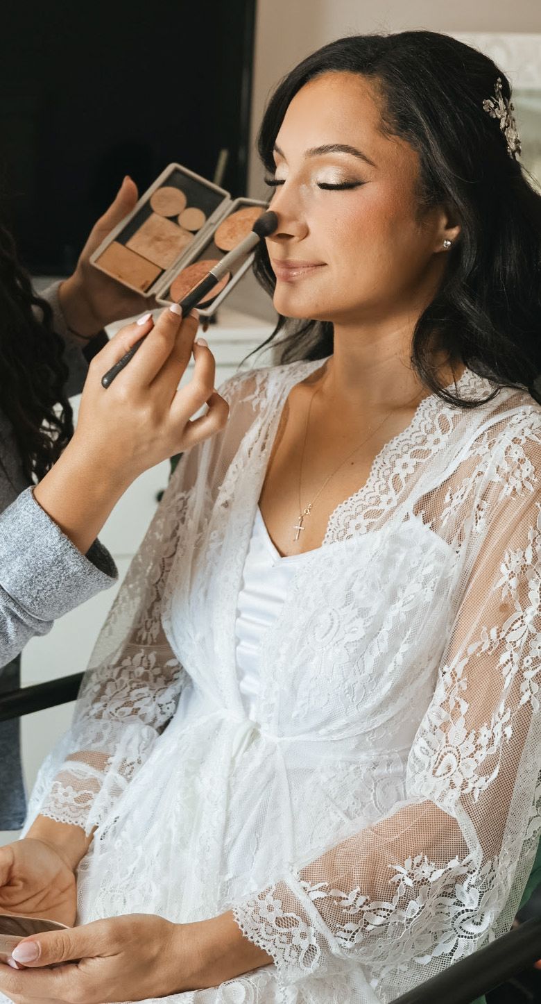 A bride in a white lace robe delicately applying perfume, capturing a quiet and elegant moment of preparation.