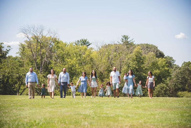 A large, multi-generational family walking together through a sun-drenched green field, capturing a legacy of love and connection.
