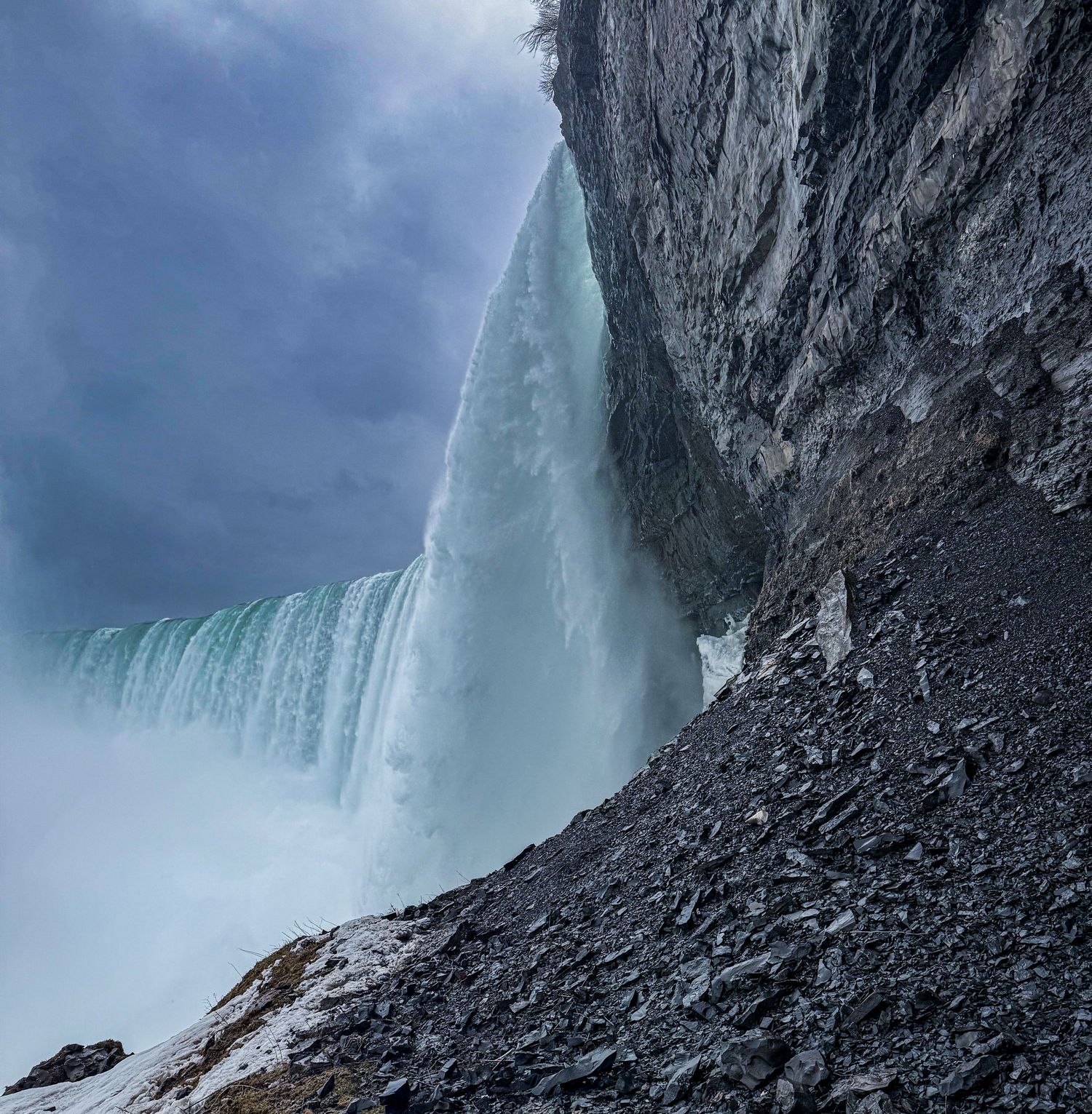 Dramatic close-up view beneath frozen Niagara Falls with rocky terrain and misty waters.