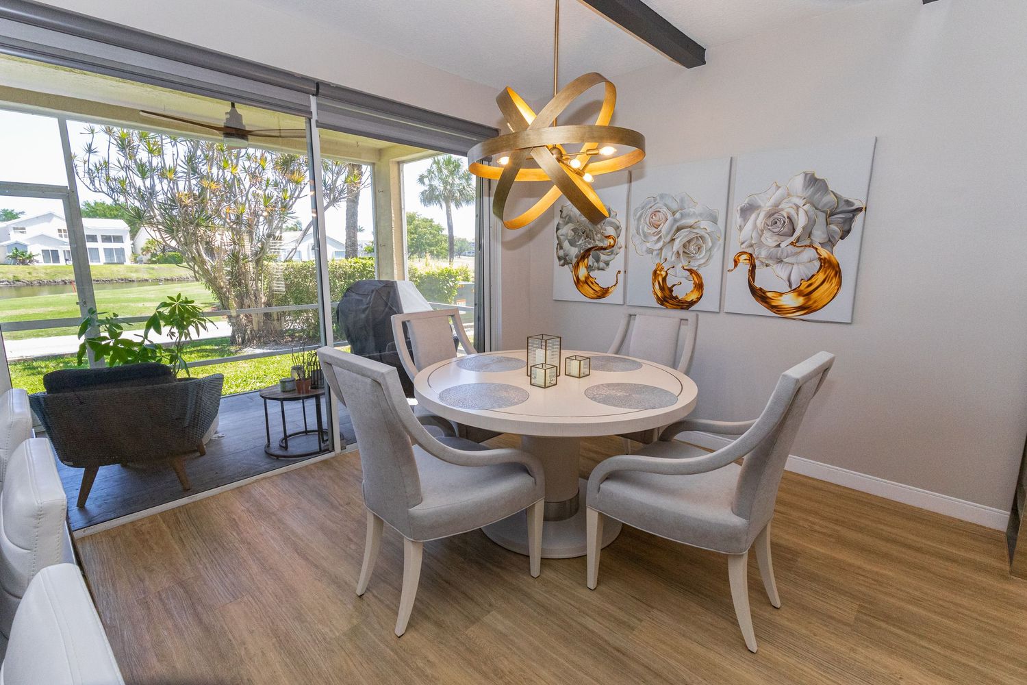 Bright dining room with round white table, gold chandelier, and large windows overlooking garden.