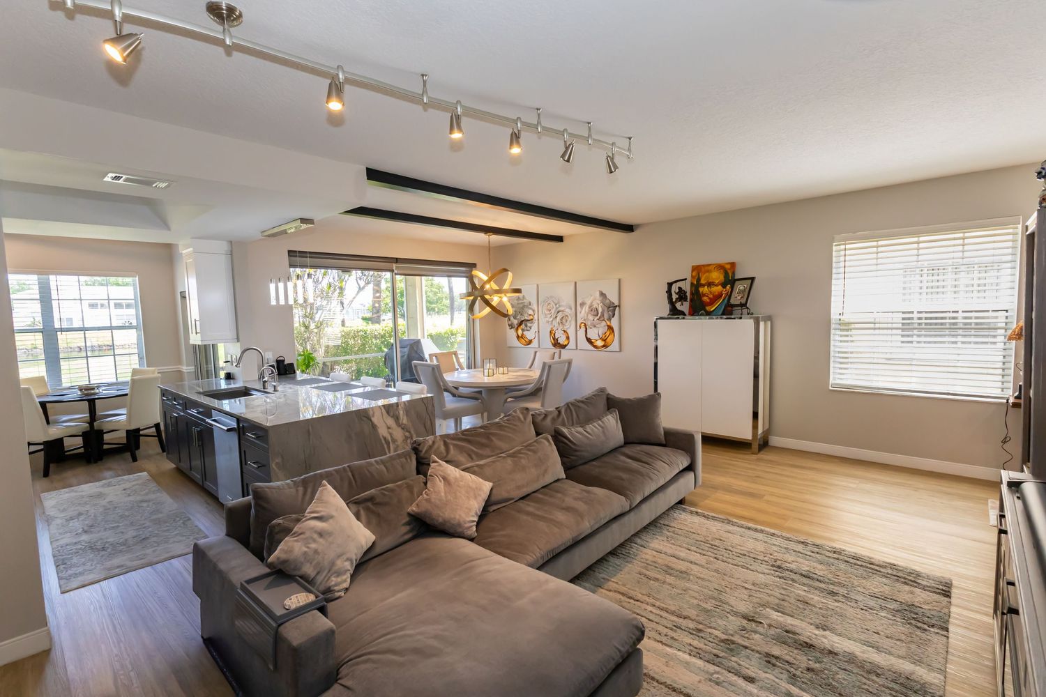 Open-concept living room with gray sectional sofa, track lighting, hardwood floors, and dining area.