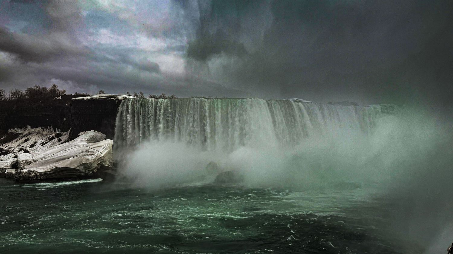 Powerful Niagara Horseshoe Falls cascading with mist rising under dark stormy winter sky.