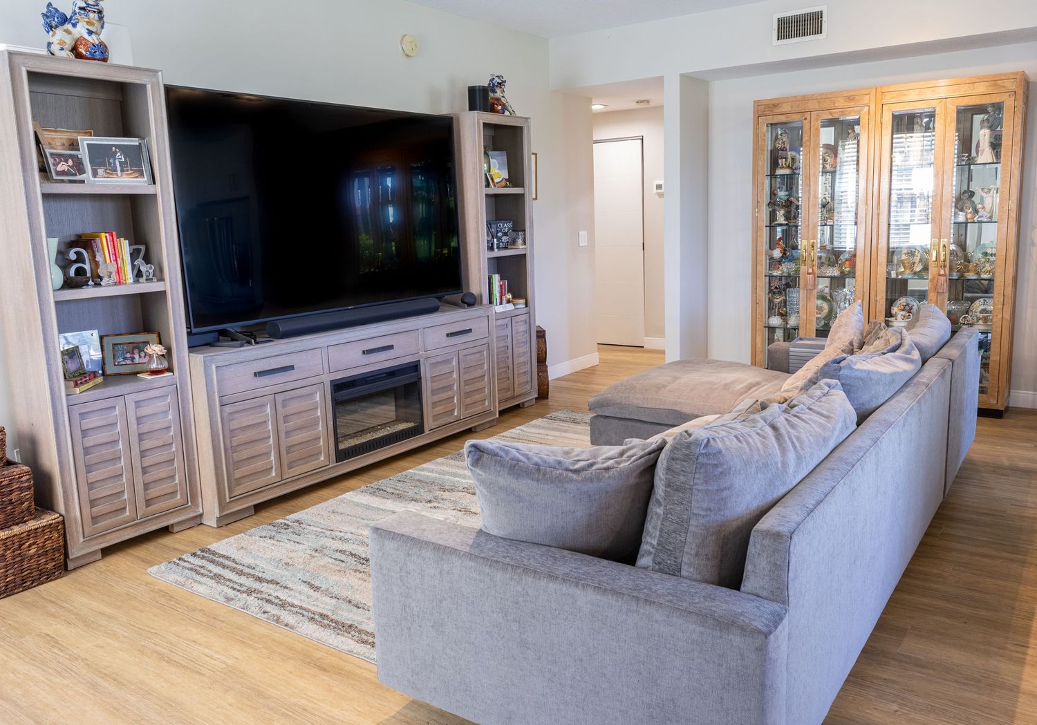 Modern living room with large wall-mounted TV, built-in shelving, fireplace, and gray sectional sofa.