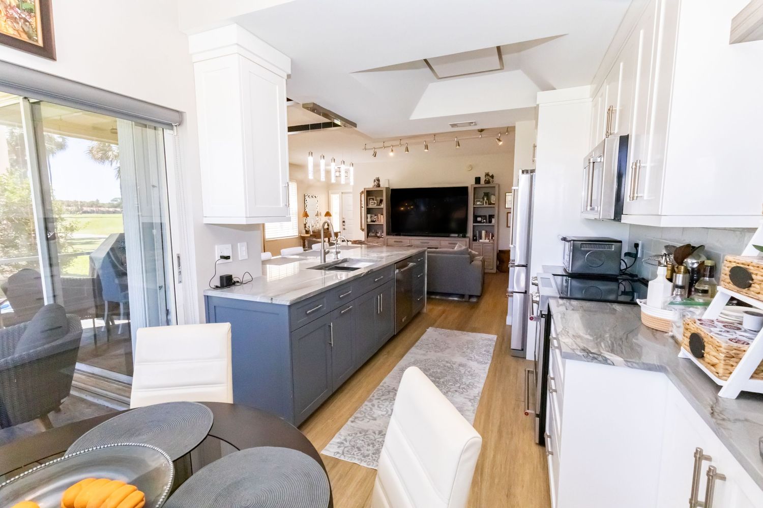 Open kitchen with gray and white cabinets, granite counters, kitchen island, and sliding glass doors.