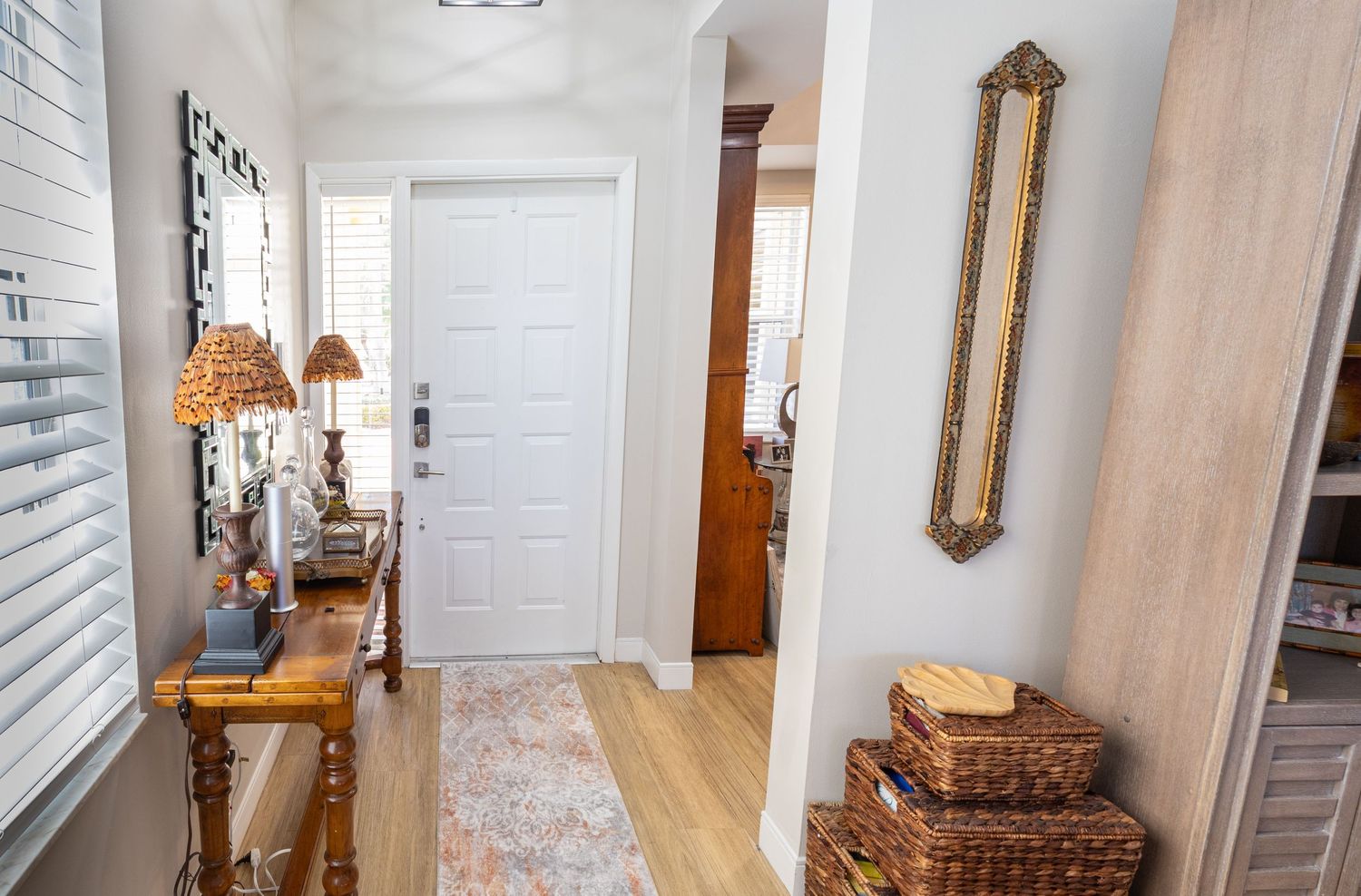 Bright home entryway with wood console table, wicker baskets, decorative mirror, and hardwood floors.