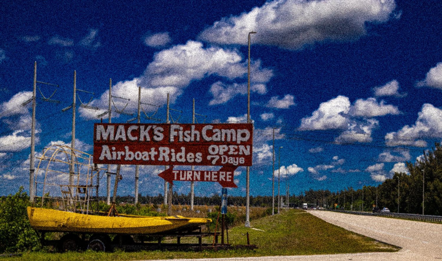 Vintage roadside sign for Macks Fish Camp and Airboat Rides open 7 days with boats displayed under a cloudy blue sky.