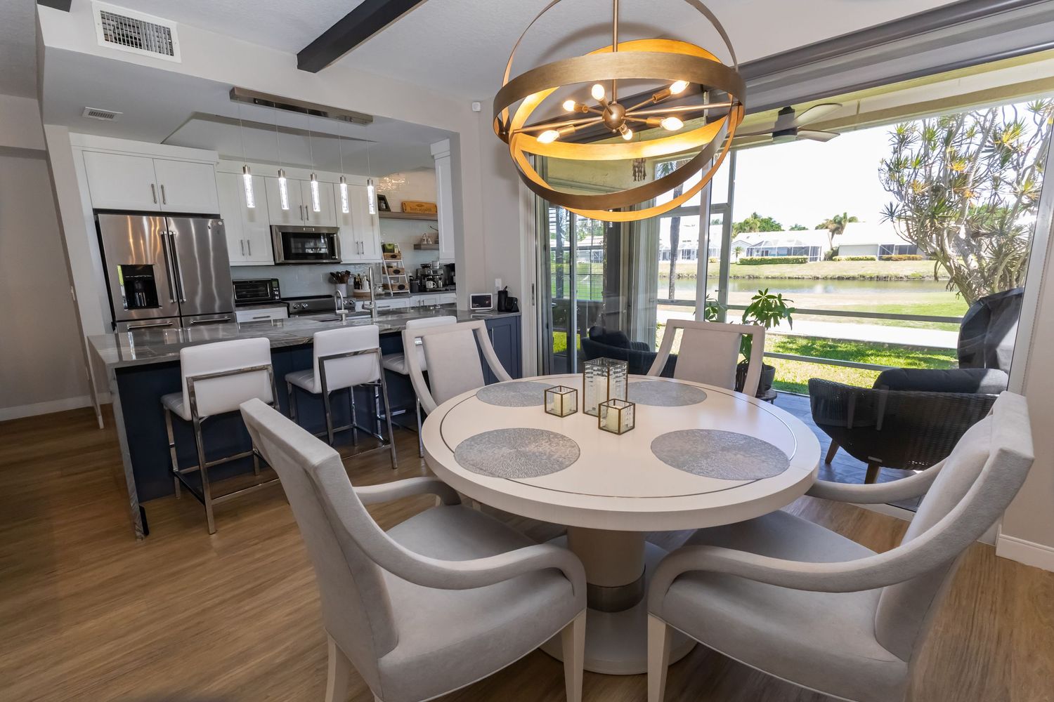 Modern dining area with round white table, gold chandelier, and open kitchen with bar seating.