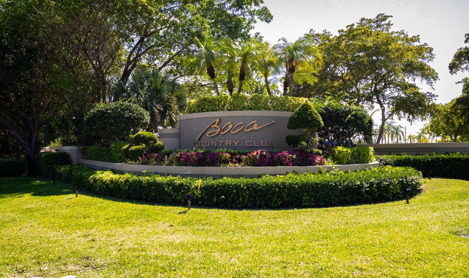 Luxury community entrance sign surrounded by tropical palms, lush green landscaping, and colorful flowers.