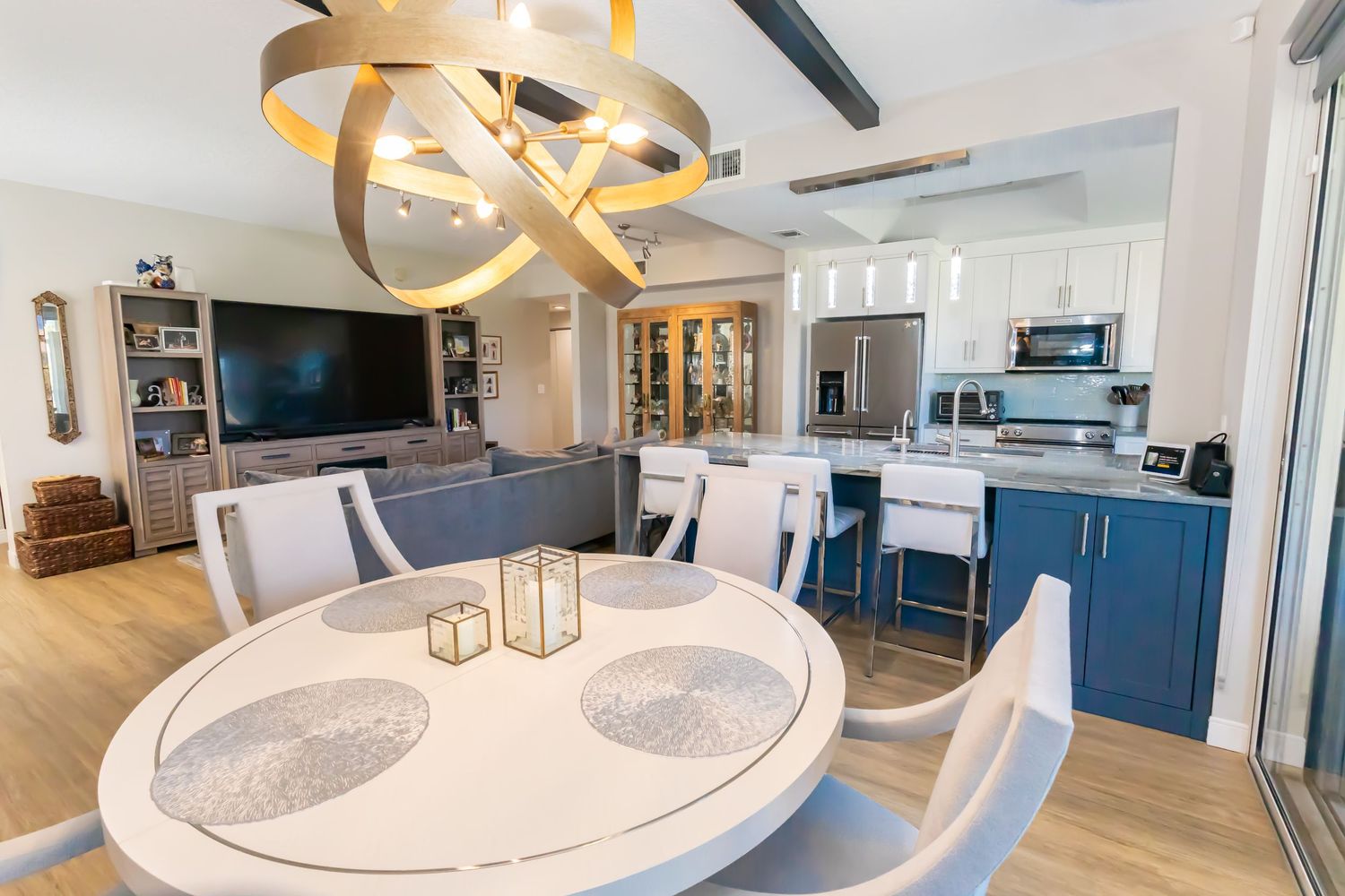 Contemporary open-plan dining and living space with blue kitchen island and gold chandelier.