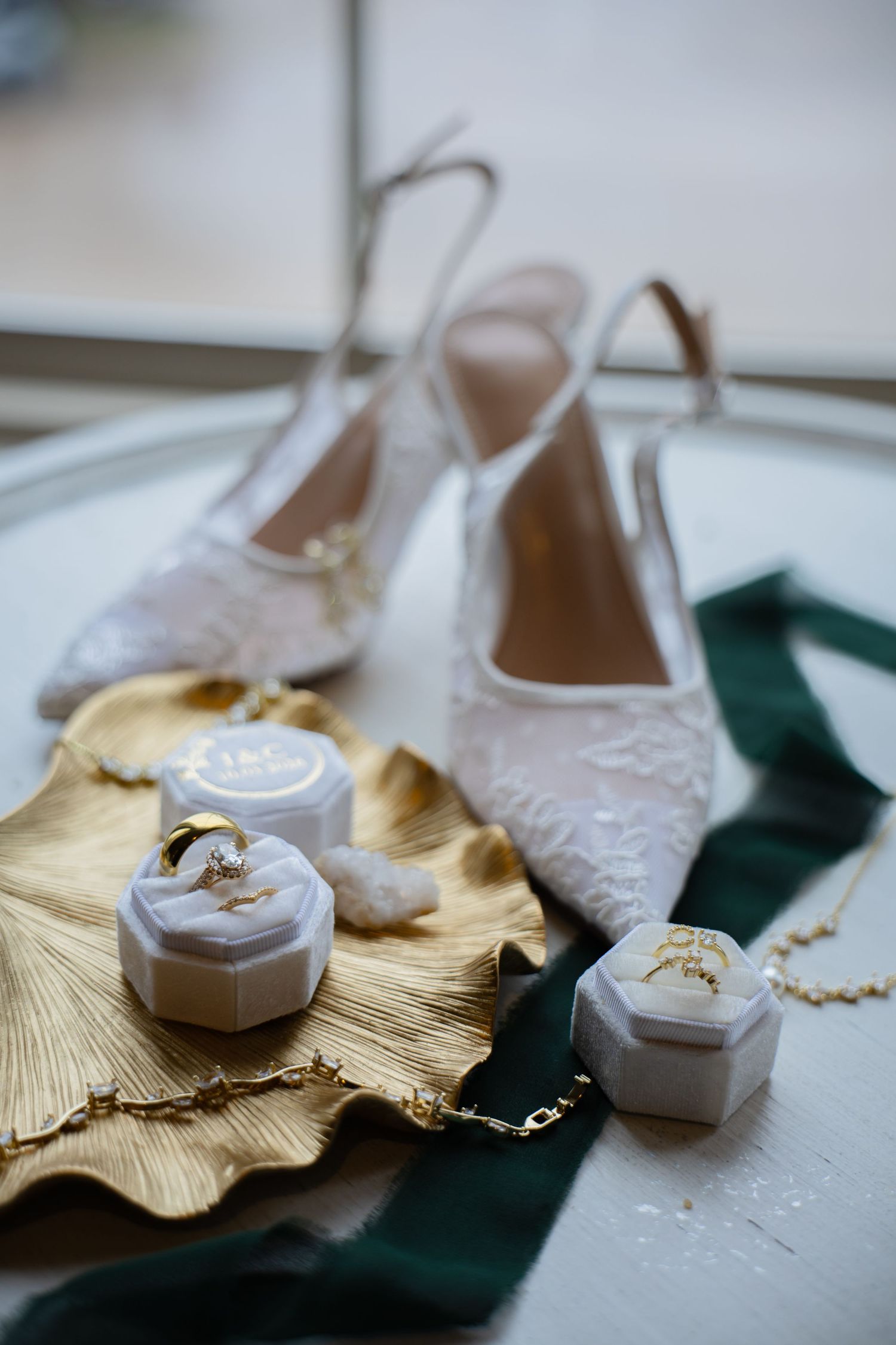 Elegant bridal accessories flat lay featuring lace heels, wedding rings in velvet boxes, and gold jewelry.
