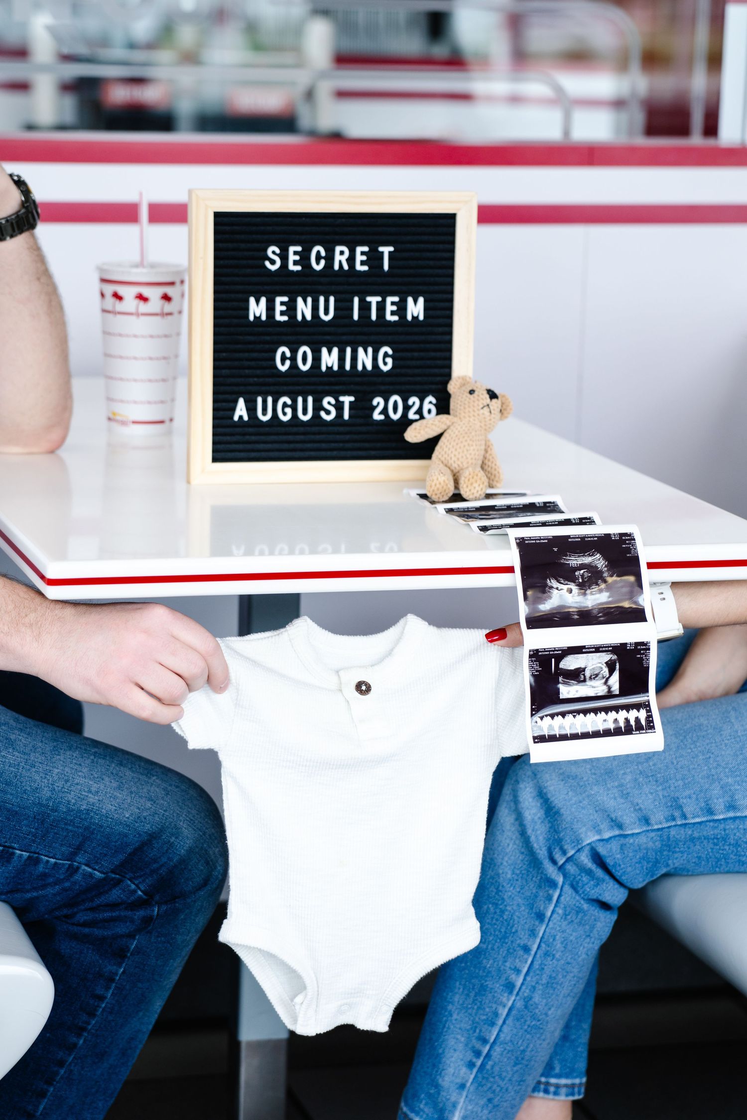 Couple at diner holding baby onesie and ultrasound photos with secret menu item pregnancy announcement sign.