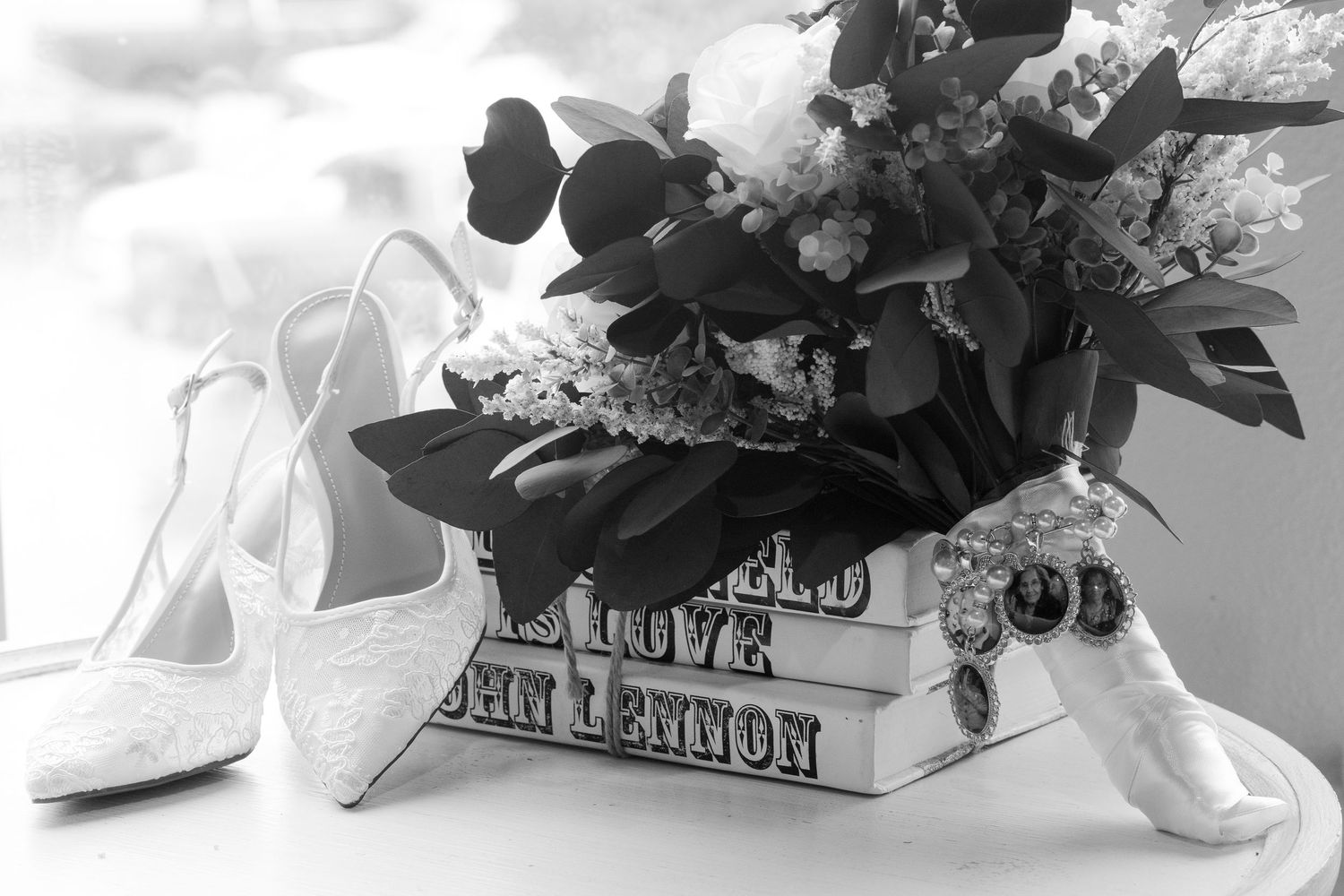 Black and white photo of bridal heels, bouquet, and accessories arranged on John Lennon books.
