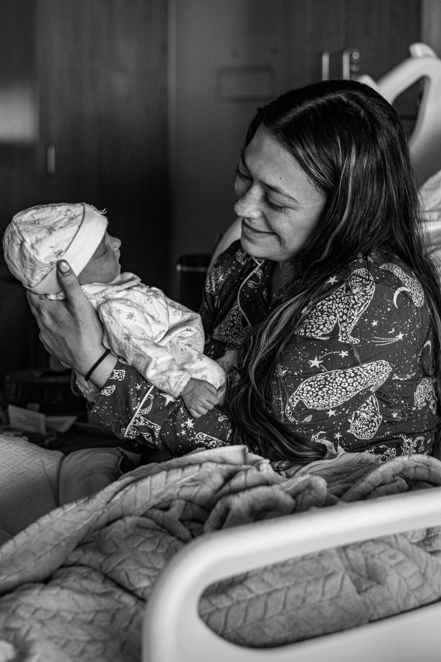 Black and white photo of a smiling new mother holding her newborn baby in a hospital bed.