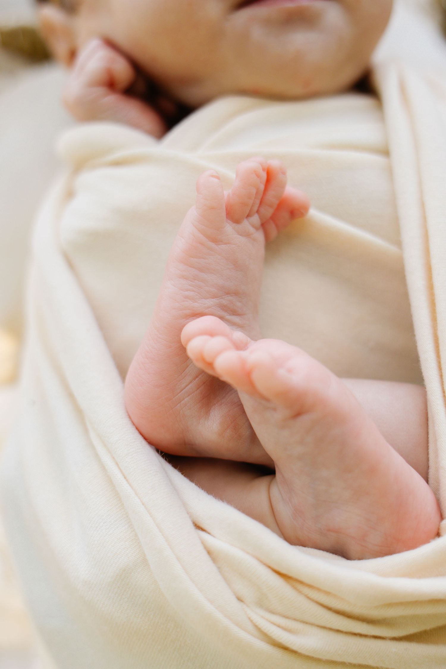 Close-up of a newborn baby's tiny feet peeking out from a soft cream swaddle blanket.