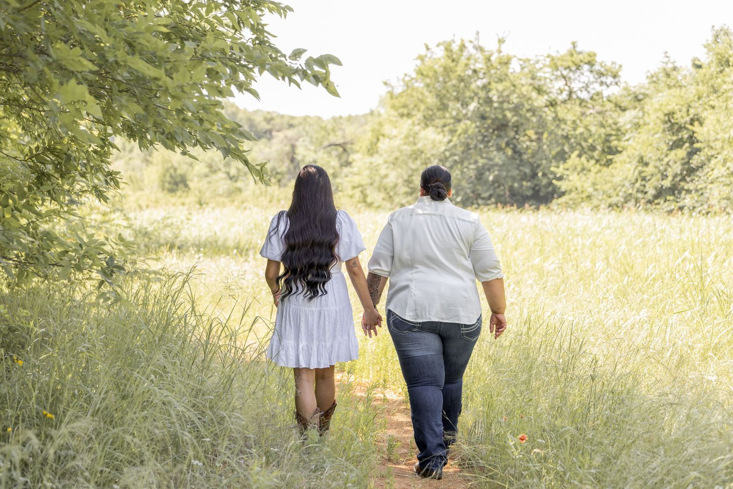 Couple walking hand in hand down a dirt path through a lush green meadow.
