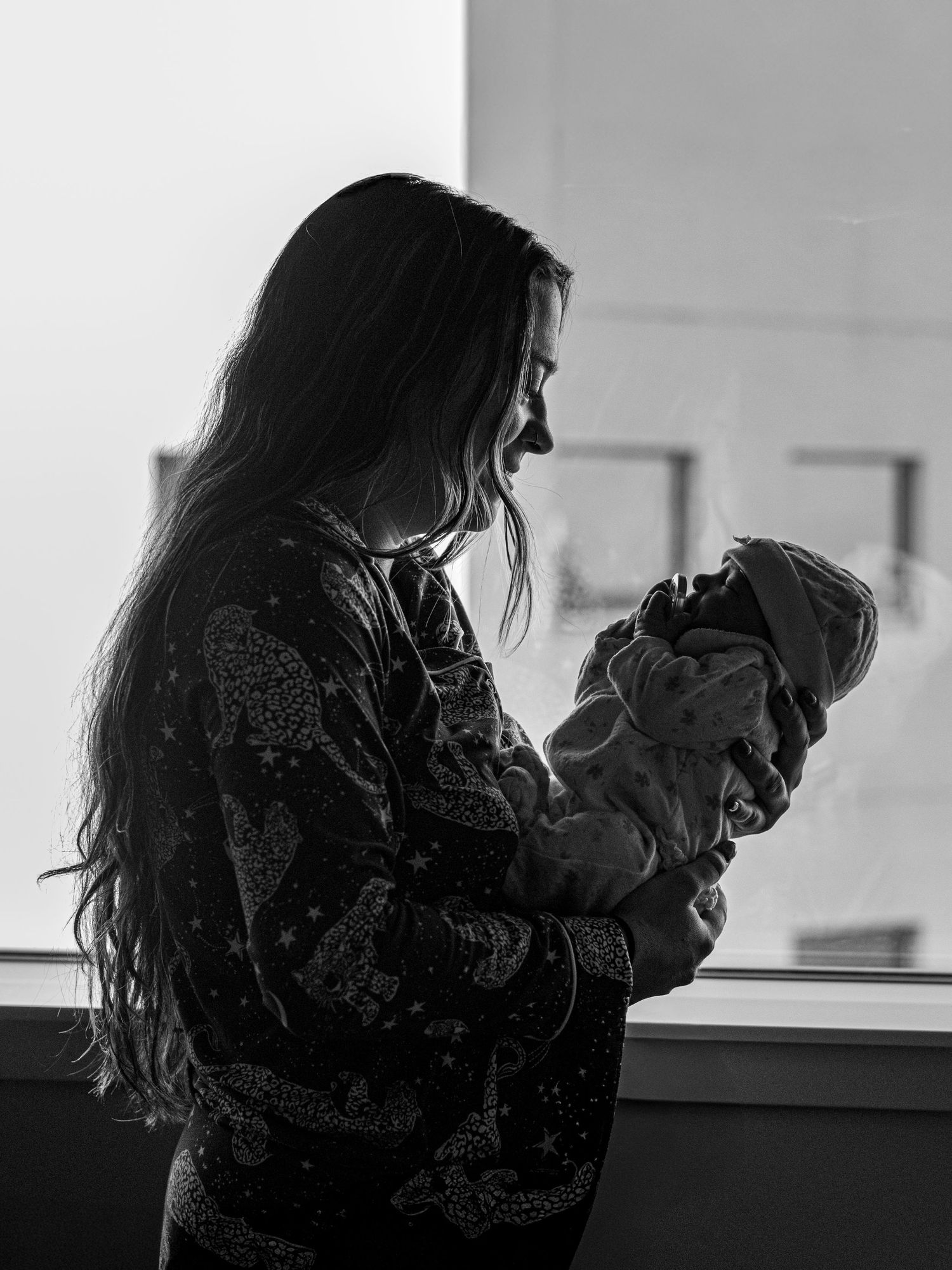 Silhouette black and white photo of a new mother holding her newborn baby near a hospital window.