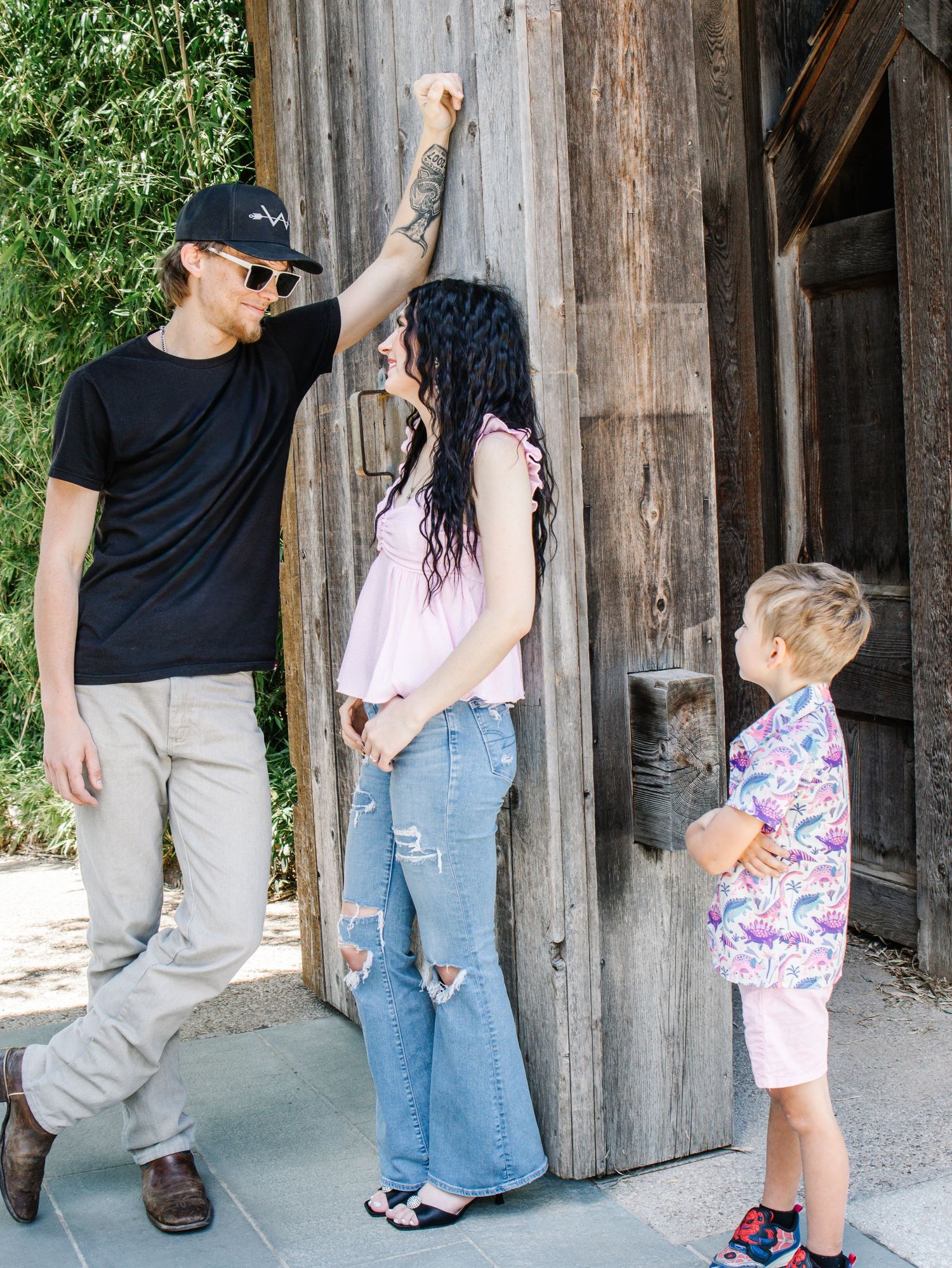 Man woman and young boy standing by a rustic wooden door outdoors in summer.