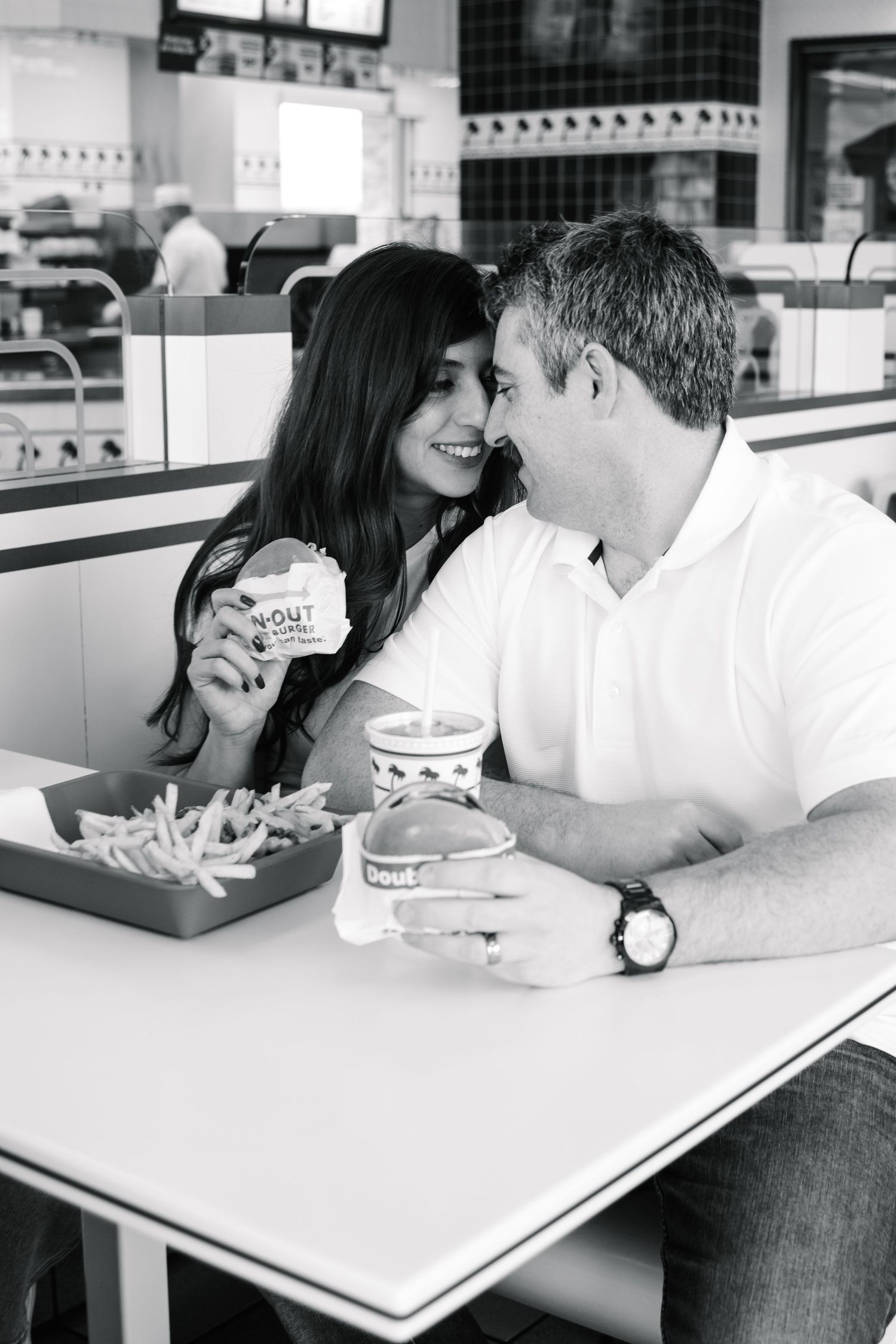 Black and white photo of a couple smiling and sharing burgers at an In-N-Out Burger restaurant.