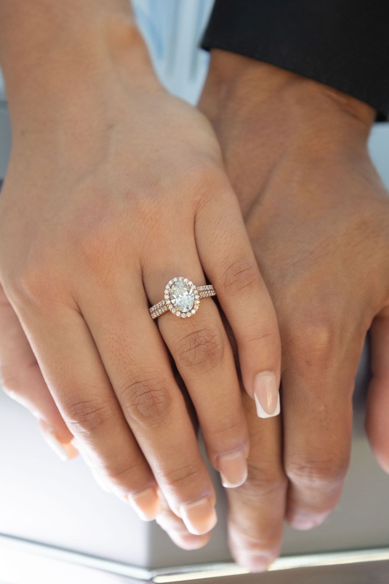 Close-up of hands wearing an elegant oval diamond halo engagement ring in rose gold with pavé band detailing.
