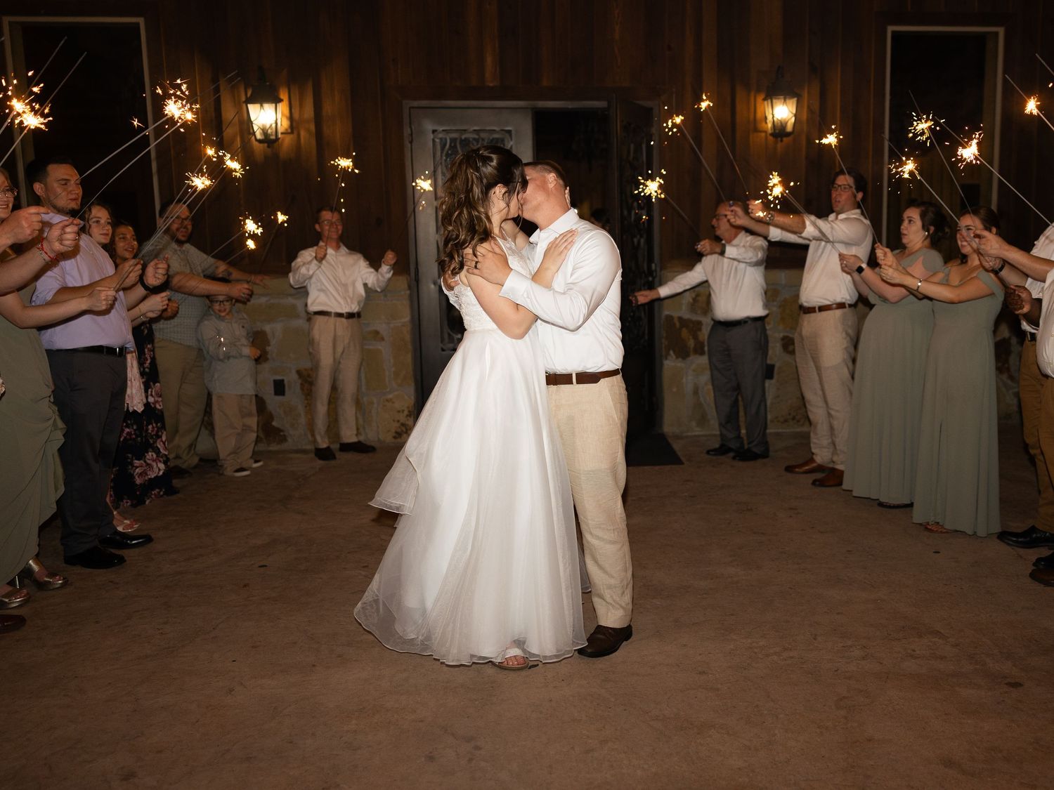 Bride and groom share first dance surrounded by guests holding sparklers at romantic rustic barn wedding reception.