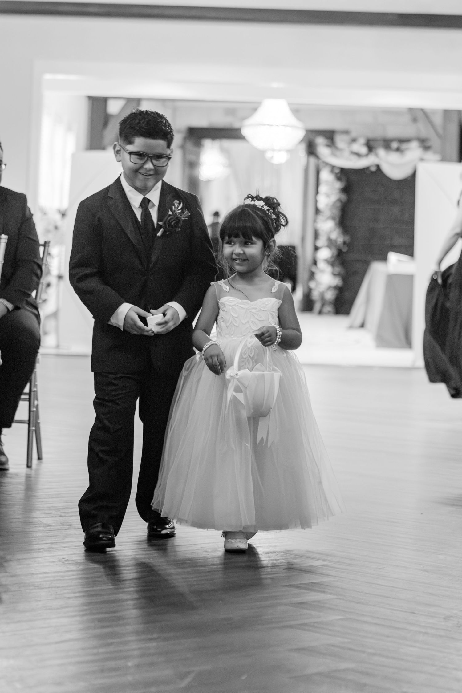 Ring bearer and flower girl walking down the aisle at a wedding ceremony in black and white.
