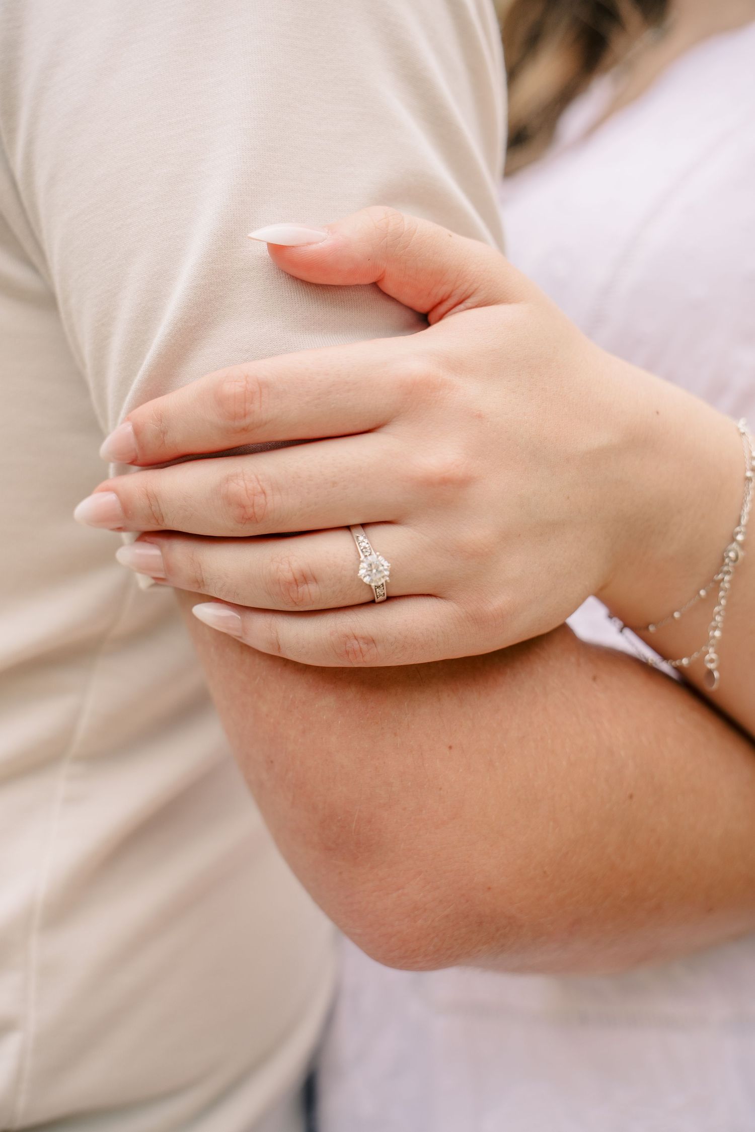 Close-up of womans hand showing diamond engagement ring while holding mans arm.