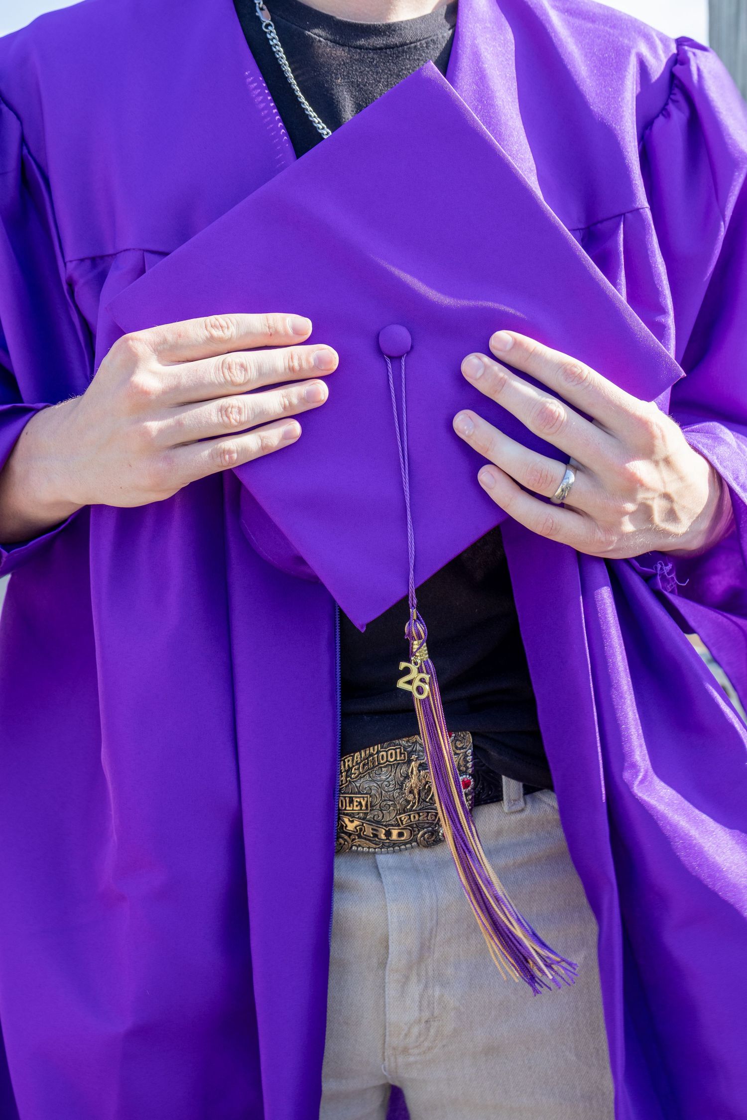 Close-up of hands holding purple graduation cap with gold tassel and ring visible.