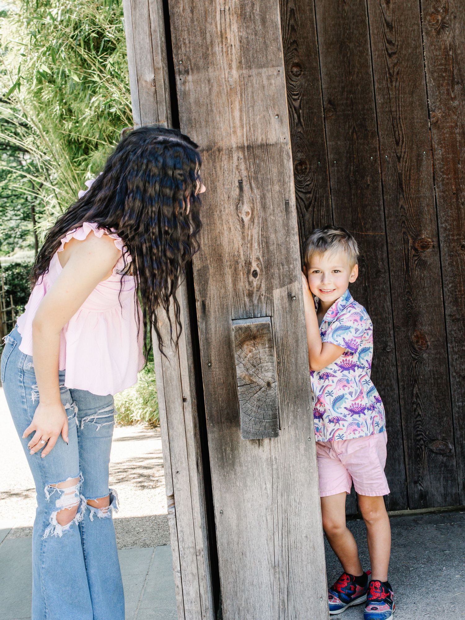 Young woman with dark braided hair and boy in colorful shirt standing by a wooden door.