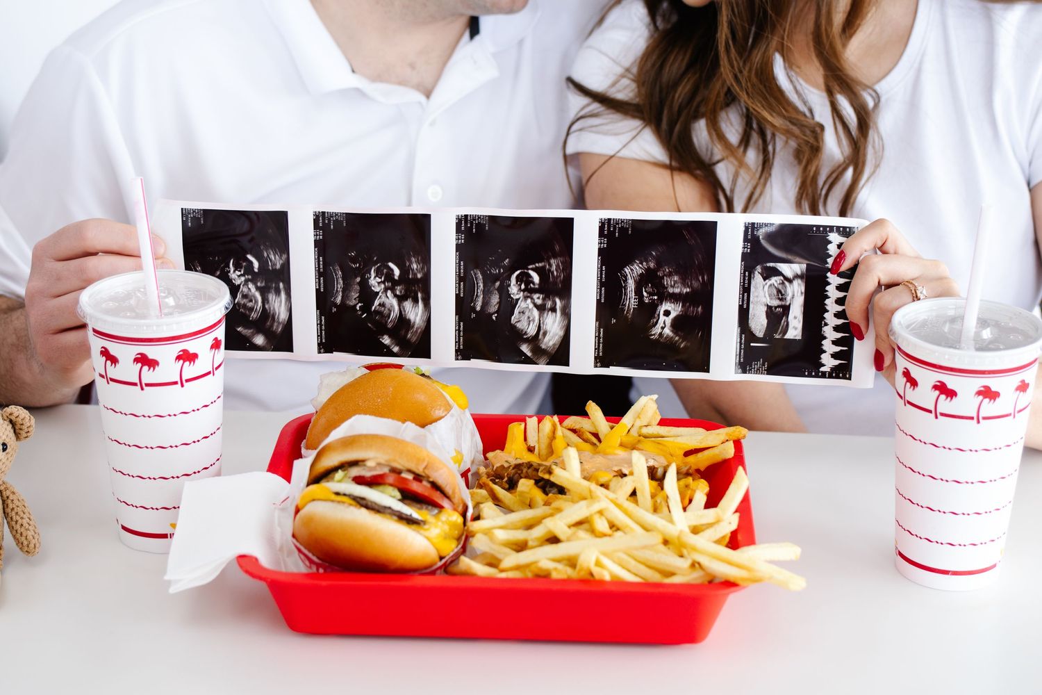 Couple at In-N-Out holding ultrasound photos over a tray of burgers and fries for pregnancy announcement.