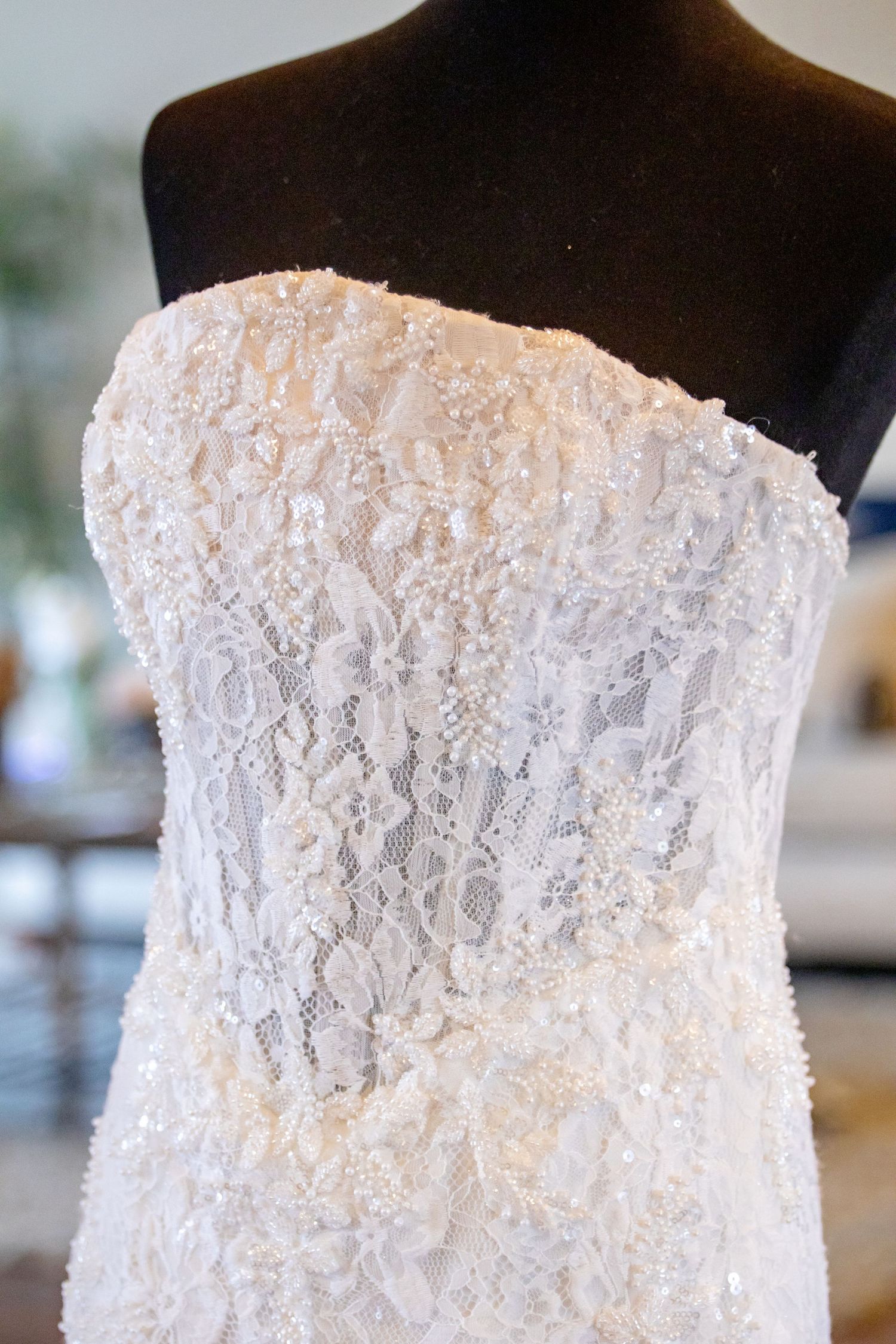 Close-up of a strapless beaded lace wedding dress bodice displayed on a black mannequin.