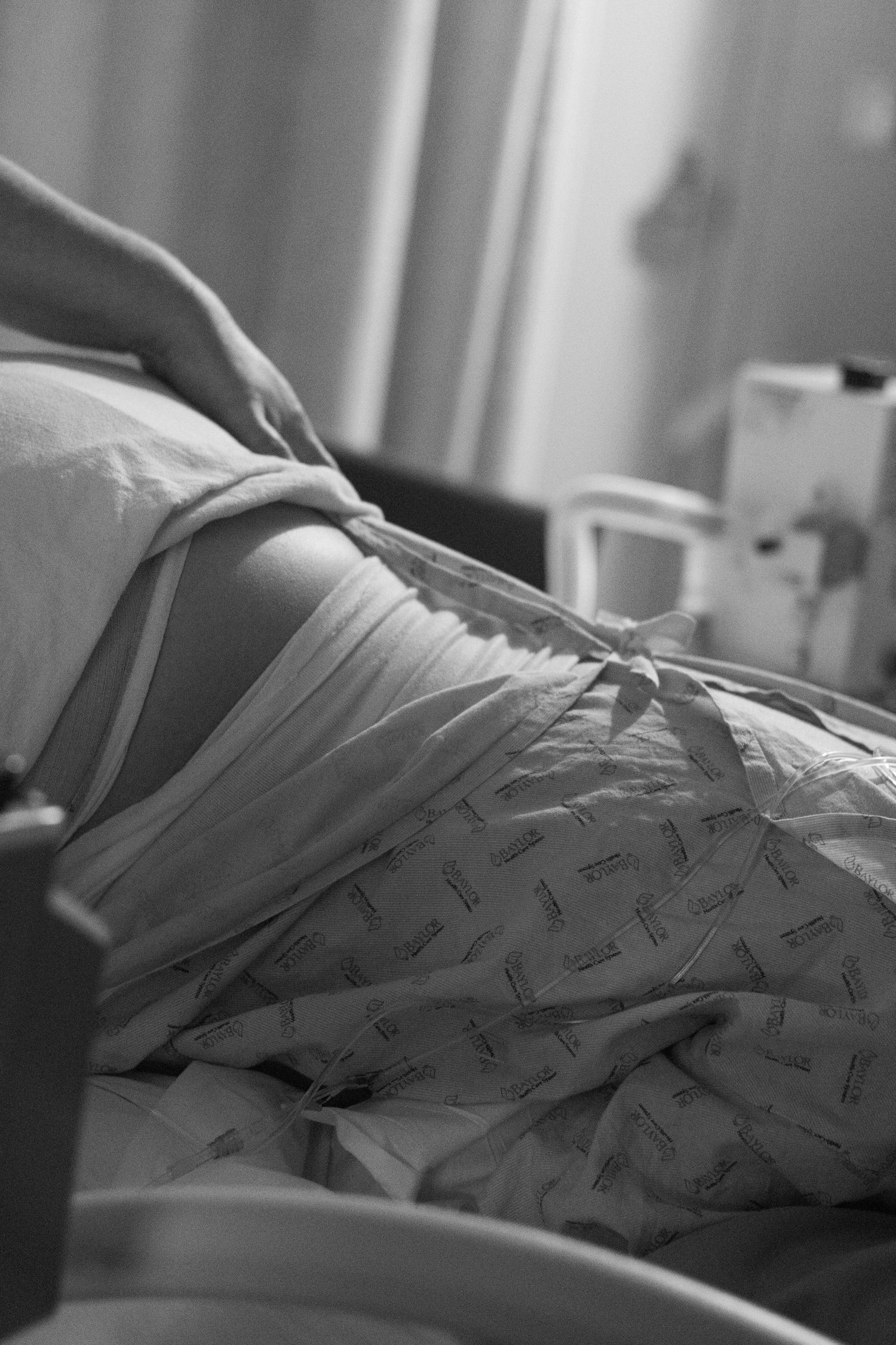 A pregnant woman in a hospital gown lies in a hospital bed during labor in black and white.