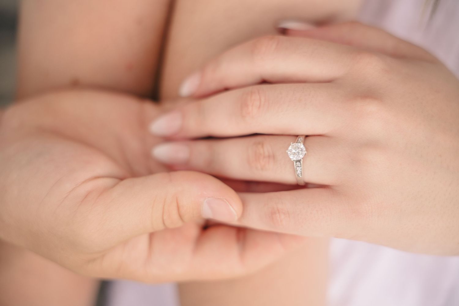 Close-up of a woman's hand wearing a elegant diamond solitaire engagement ring on her ring finger.