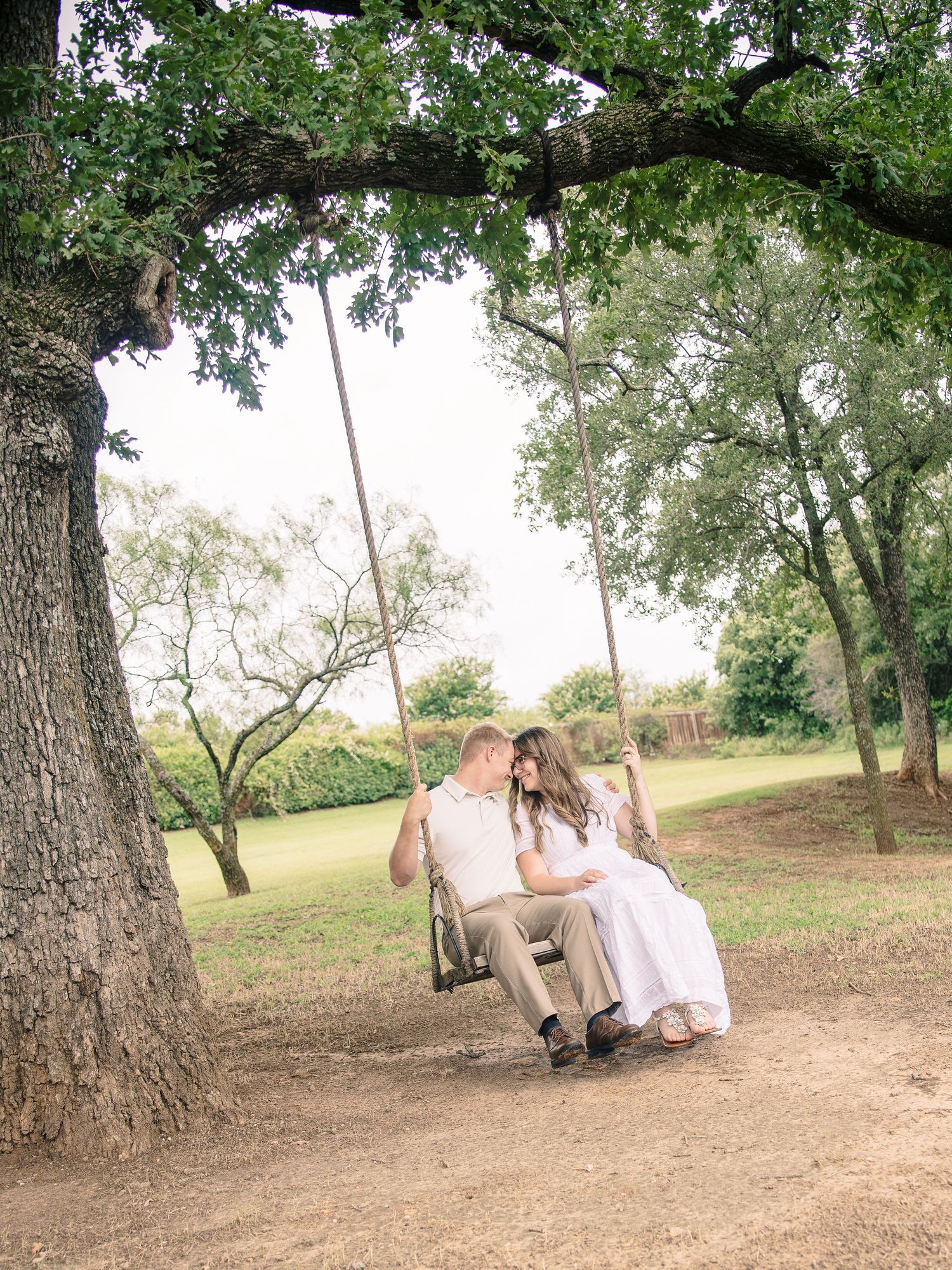 Couple sitting together on a wooden tree swing in a lush green park, sharing a romantic moment outdoors.