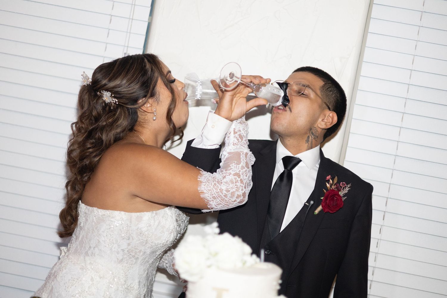 Bride and groom sharing a drink together at their wedding reception, with a white wedding cake in the foreground.