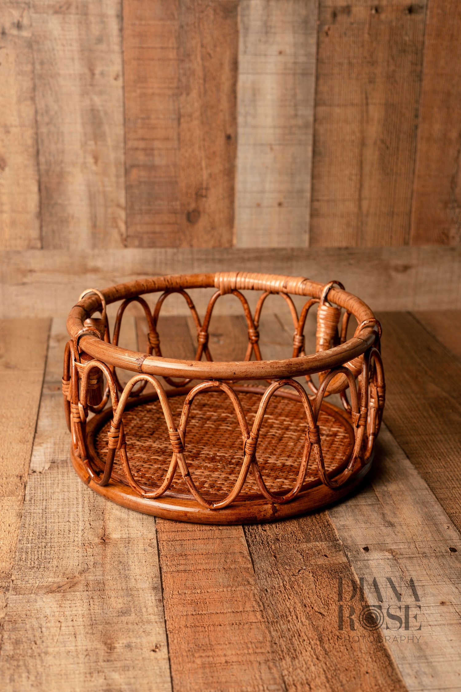 Round rattan wicker basket prop on rustic wood floor, perfect for newborn photography sessions.