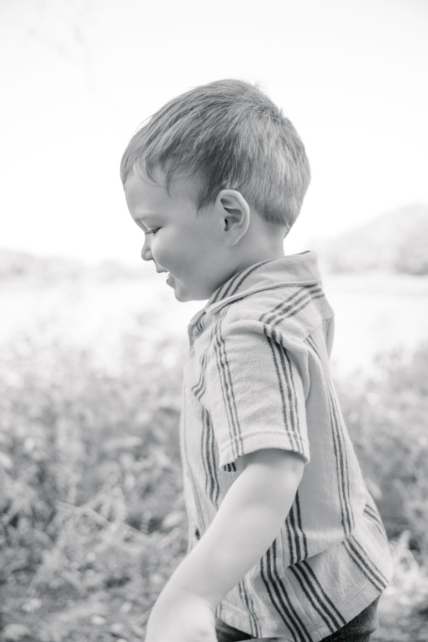 Black and white portrait of a smiling young boy in a striped shirt playing outdoors in a field.