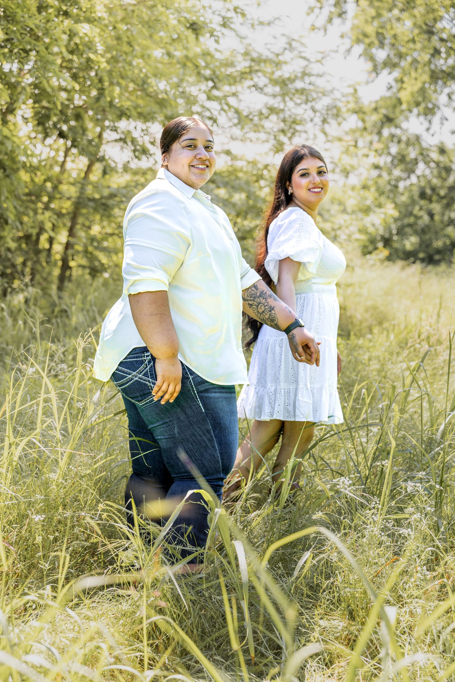 Smiling couple standing back-to-back in a lush green field on a sunny day.