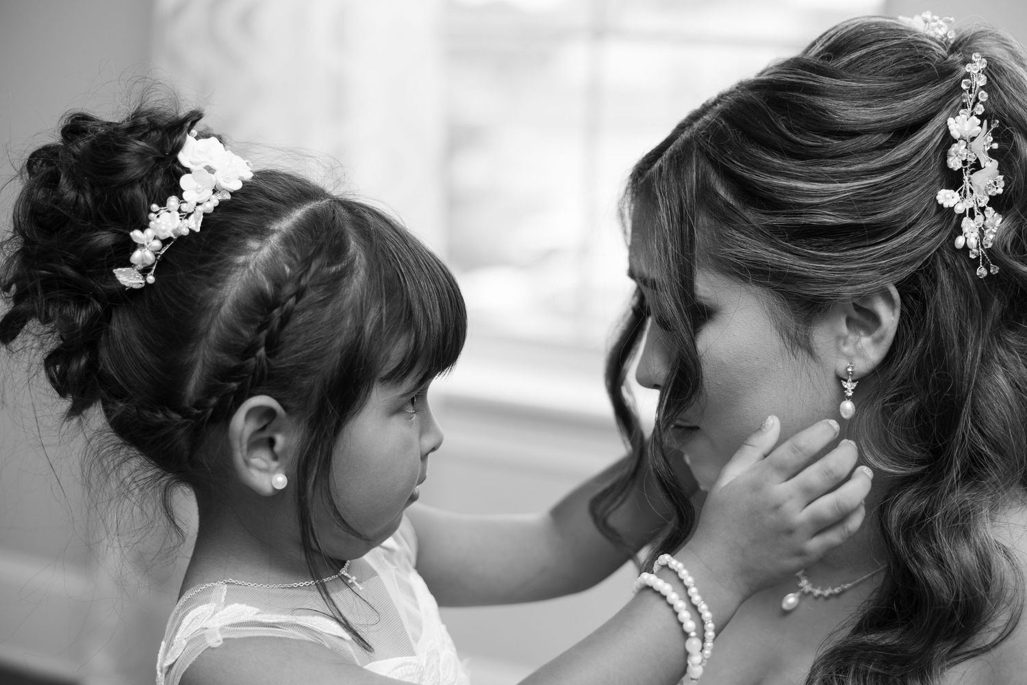 Tender black and white moment of flower girl touching brides face at wedding.