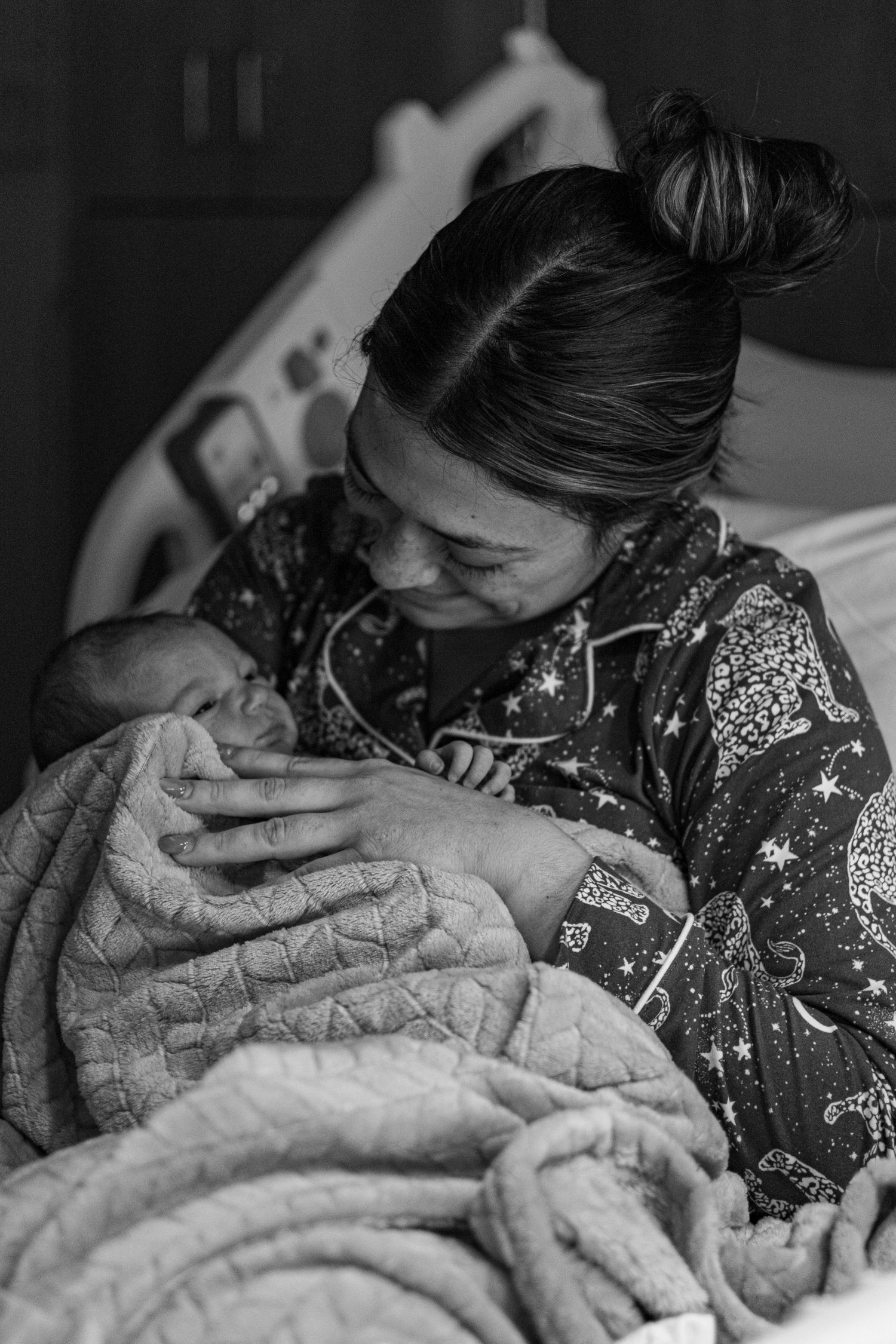 New mother smiling and cradling newborn baby in hospital bed, black and white photo.