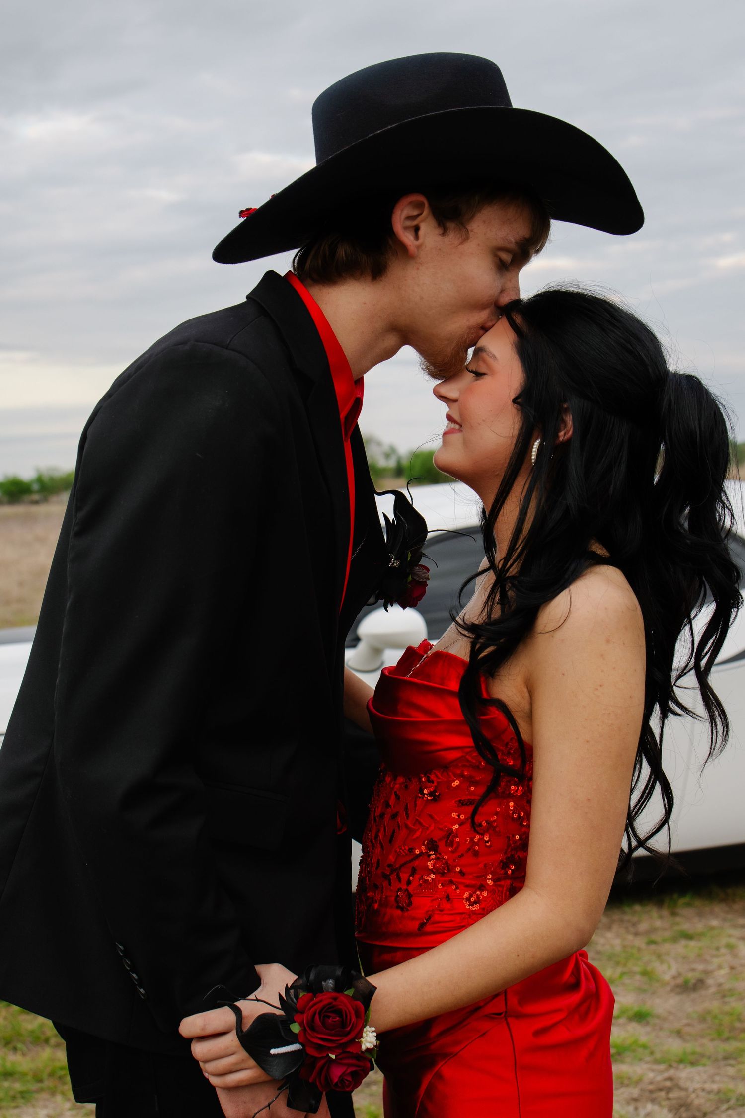 Teenage prom couple almost kissing, girl in red sequin dress, boy in black suit and cowboy hat.