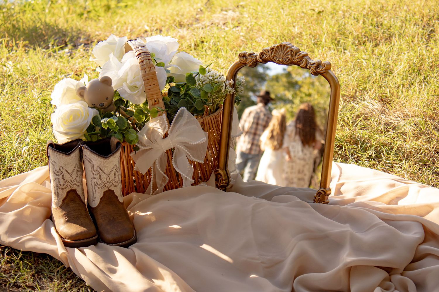 Boho maternity flat lay featuring cowboy boots, white floral bouquet in a basket, and a vintage mirror showing a couple.