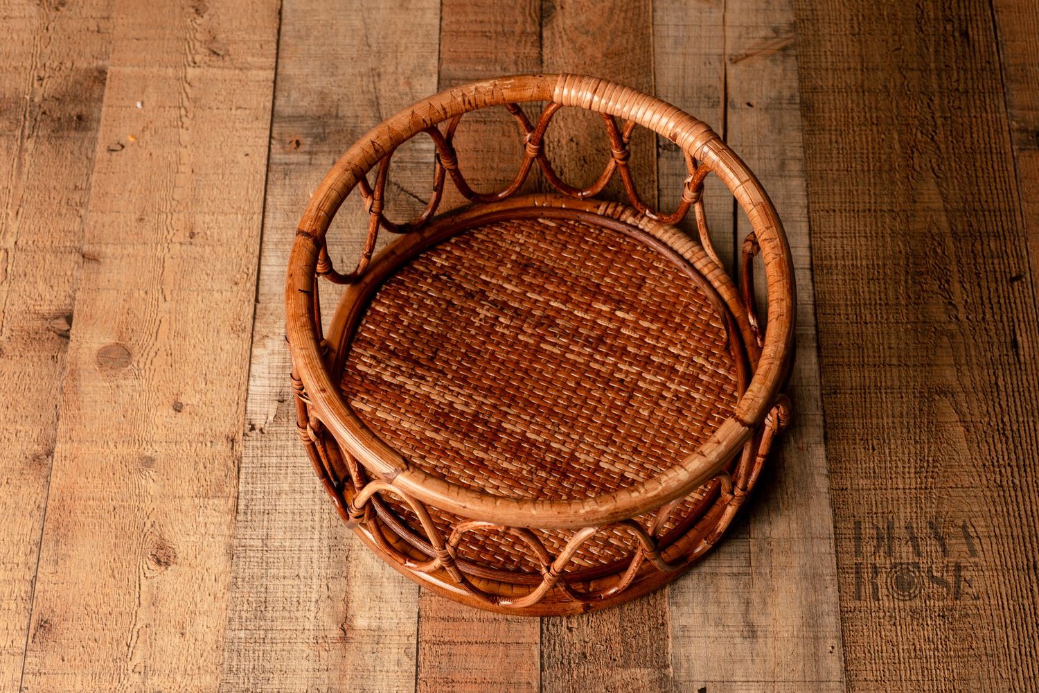 Round woven rattan basket tray with decorative looped edges on rustic wooden floor background.