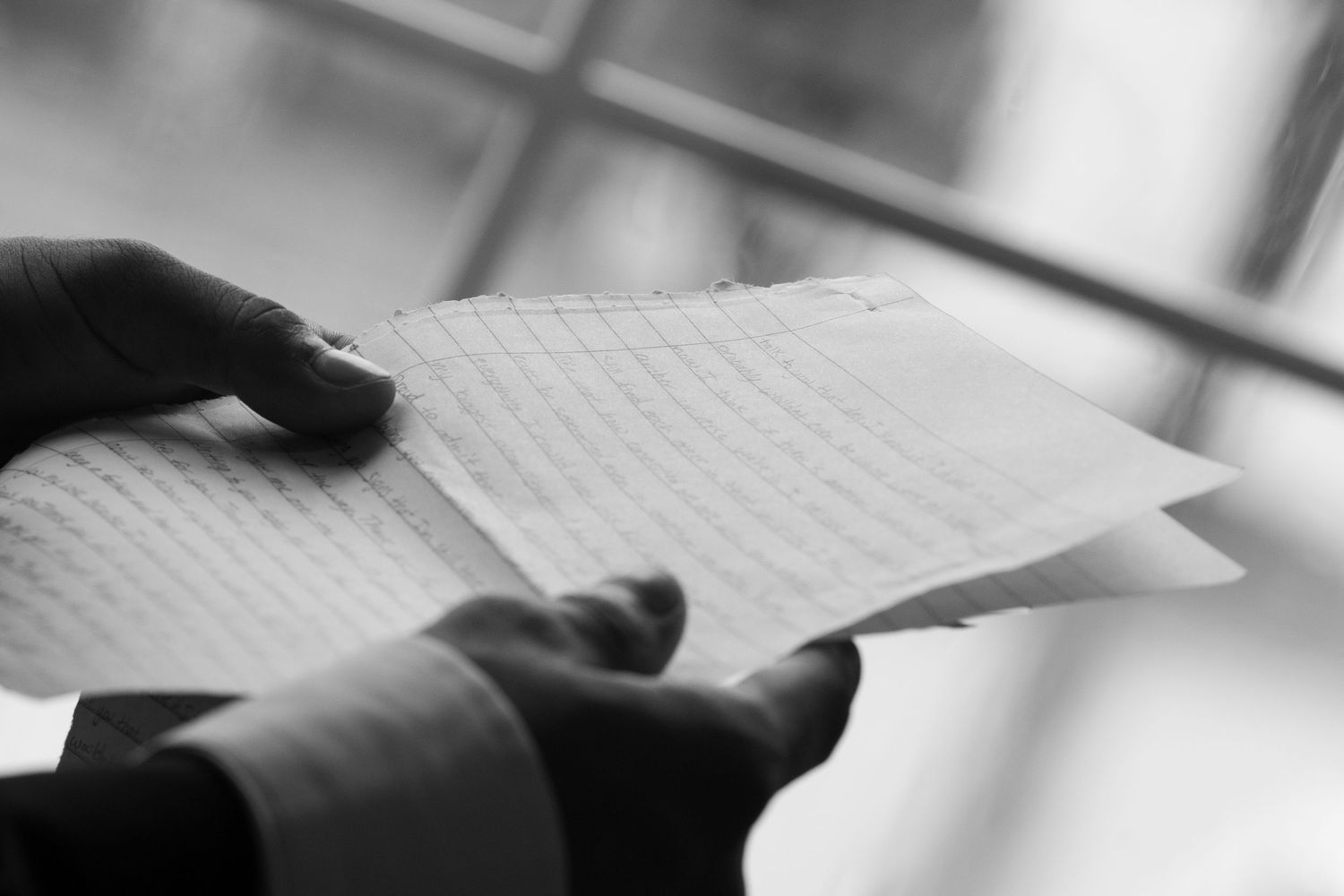 Close-up black and white photo of groom reading handwritten wedding vows letter before ceremony.