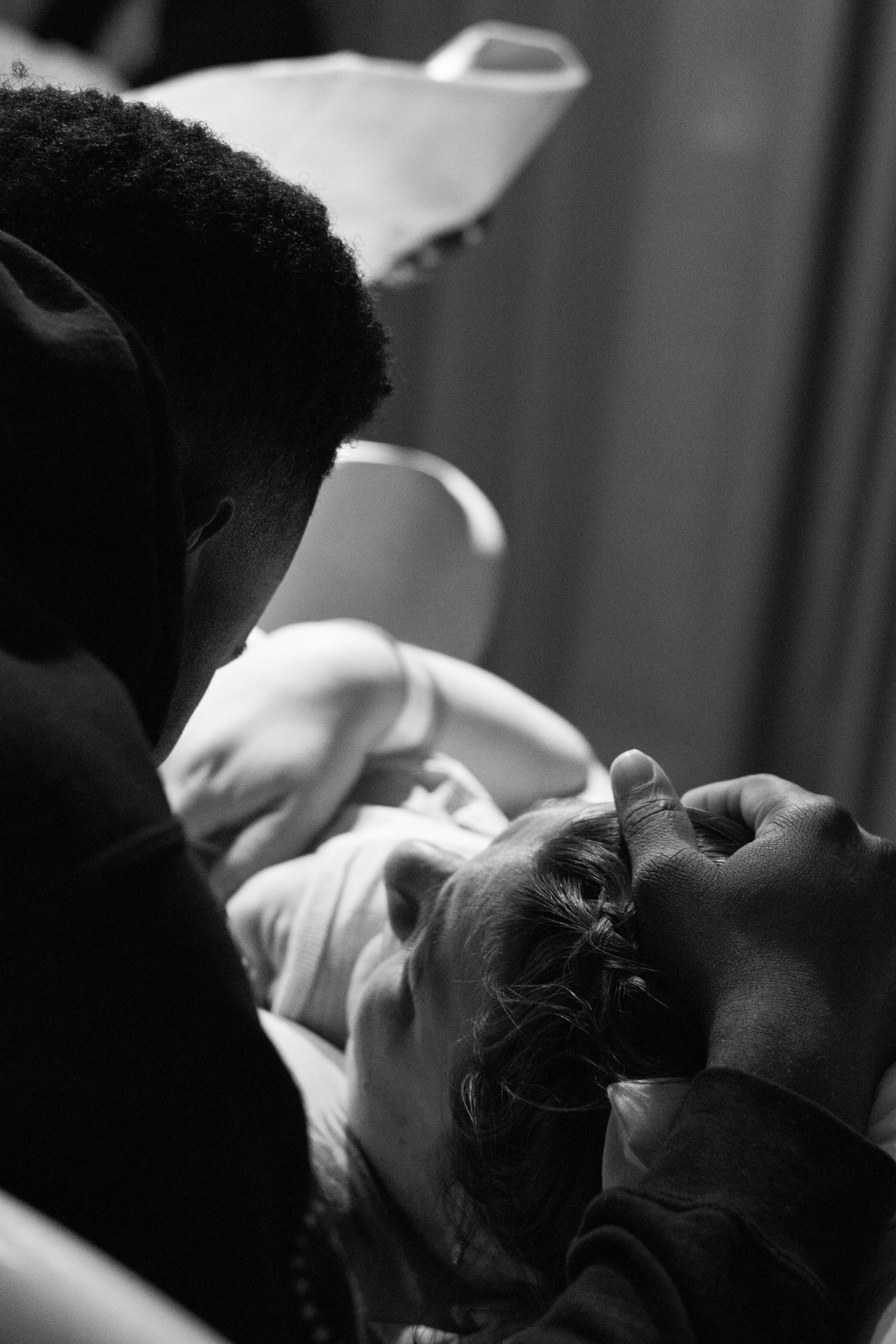 A father leans in to meet his newborn baby for the first time in a tender black and white photo.